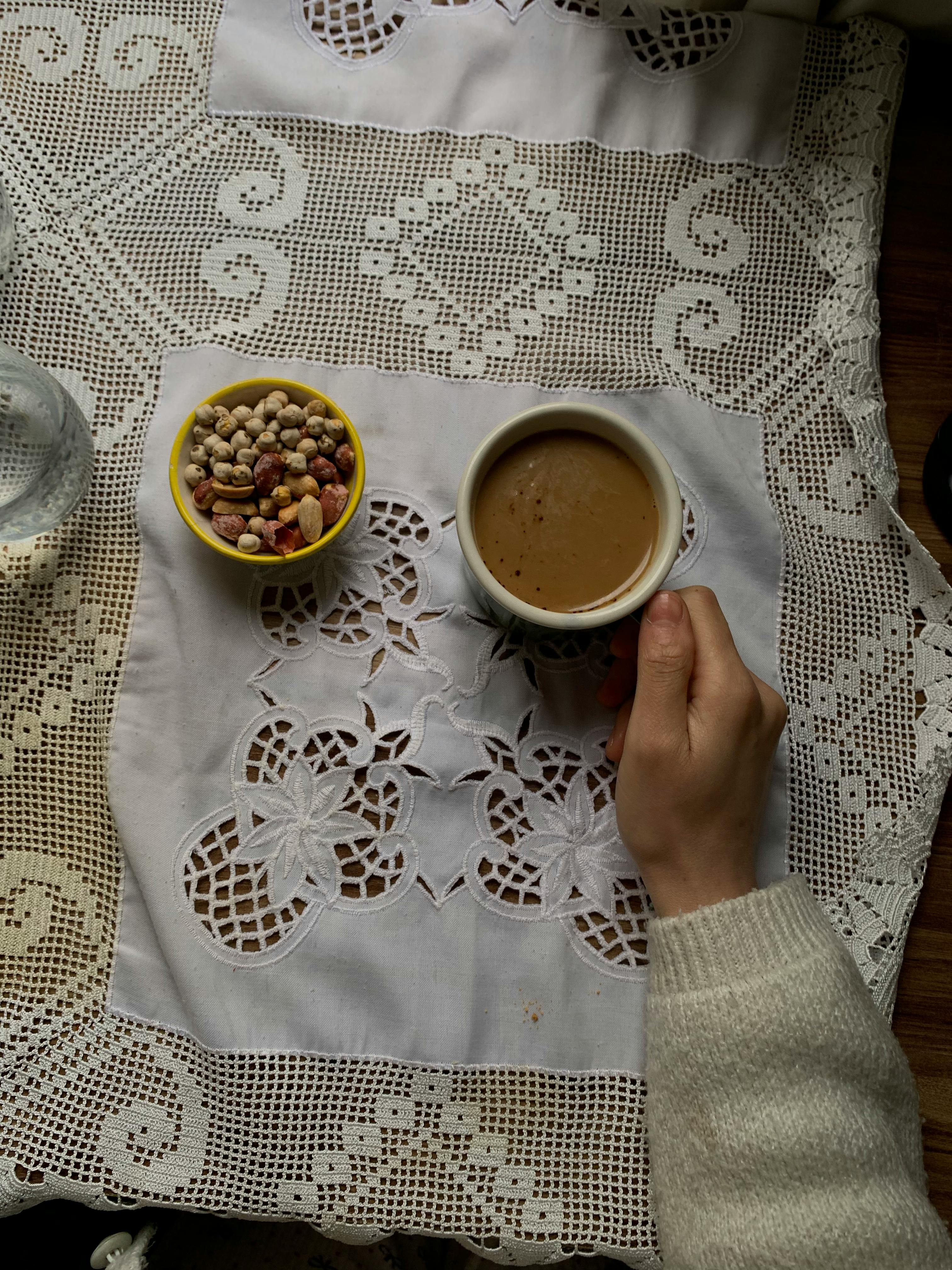 Miễn phí Không gian buổi sáng ấm áp với một tách cà phê và một bát hạt trên chiếc khăn trải bàn ren. Ảnh lưu trữ