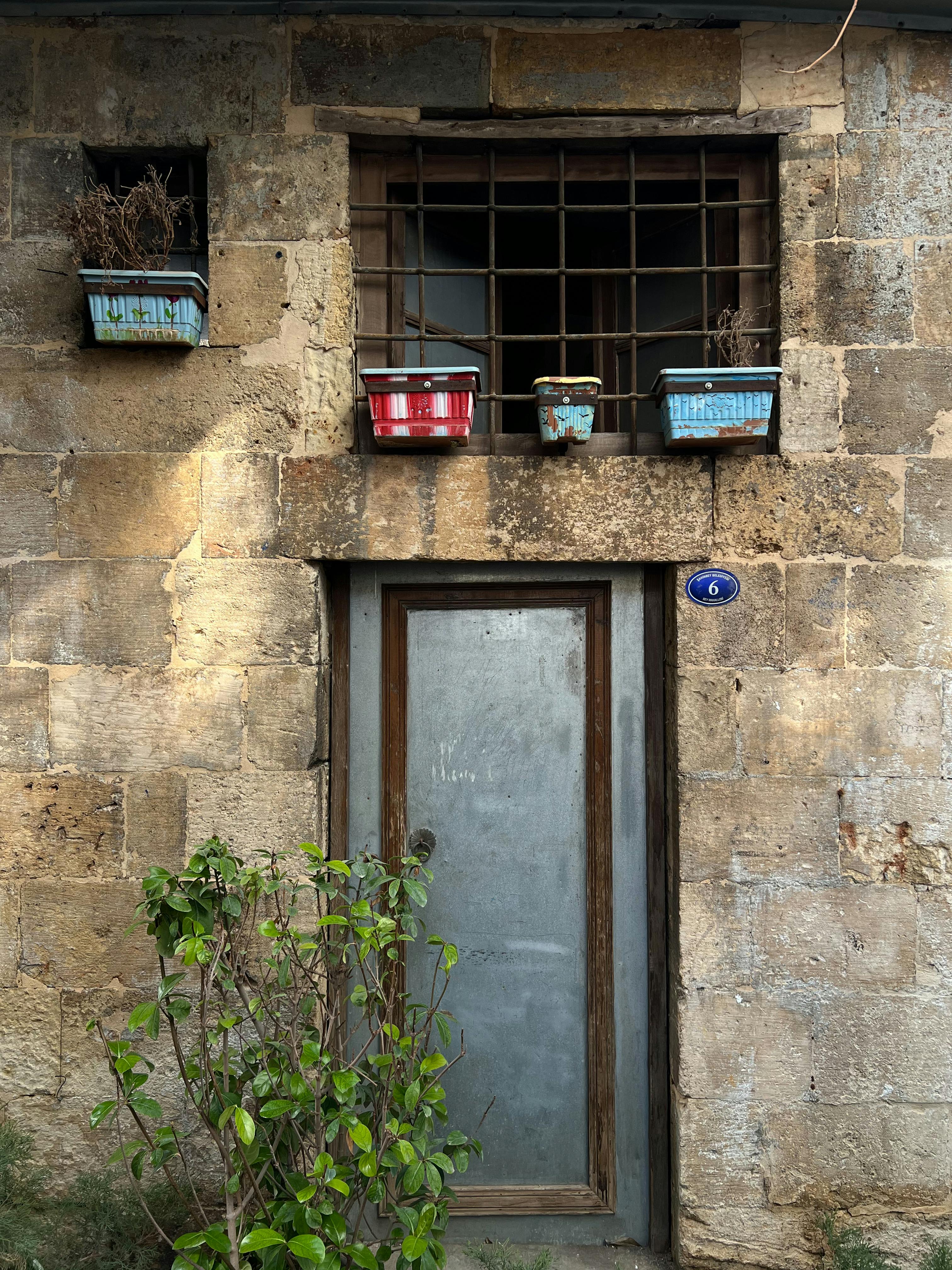 Ücretsiz Eski, rustik taş cephe, metal kapı ve gün ışığında saksı bitkileri. Stok Fotoğraflar