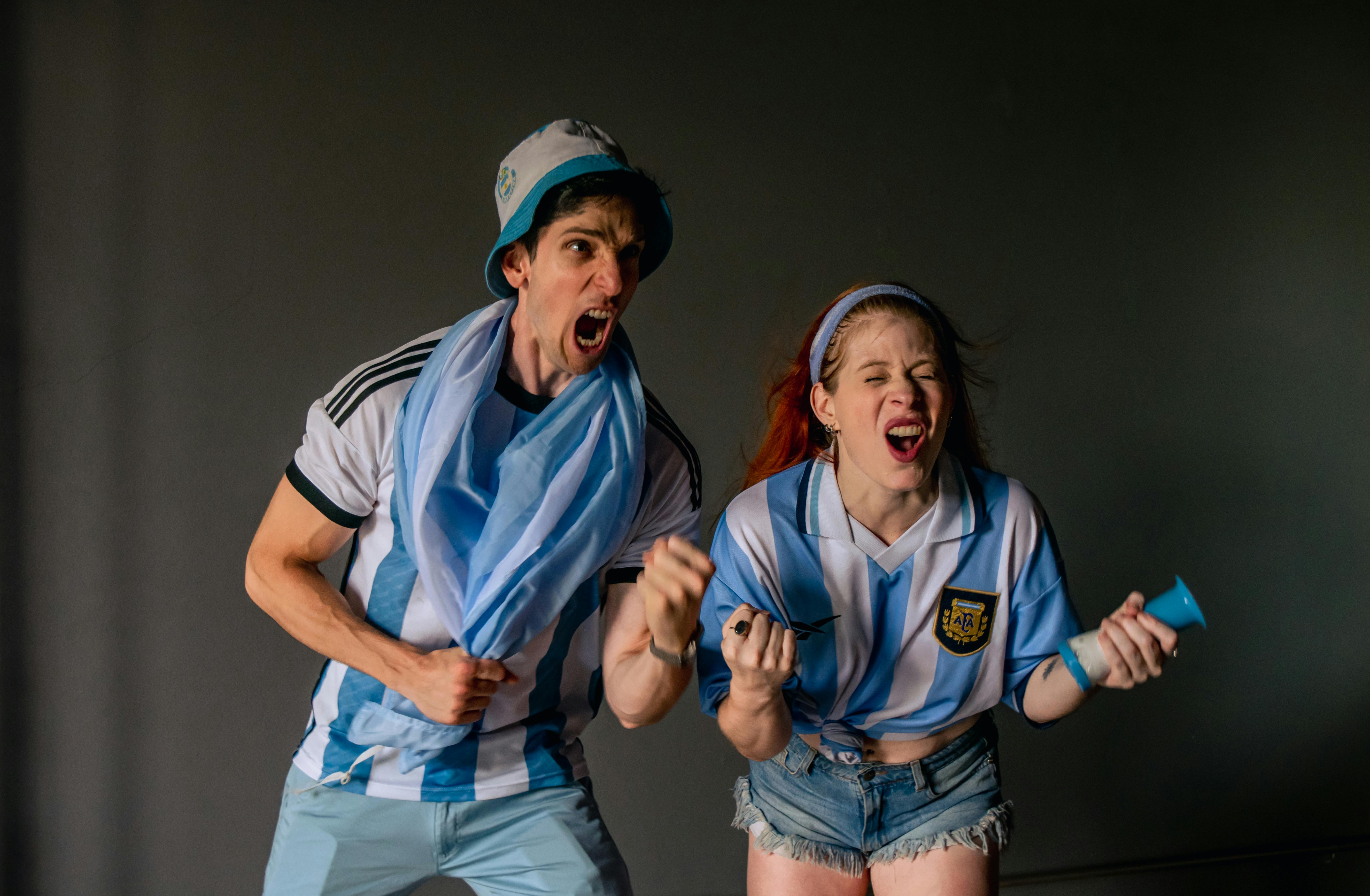 無料 アルゼンチンのジャージを着た熱狂的なファン2人が、屋内で元気よく応援している。 写真素材