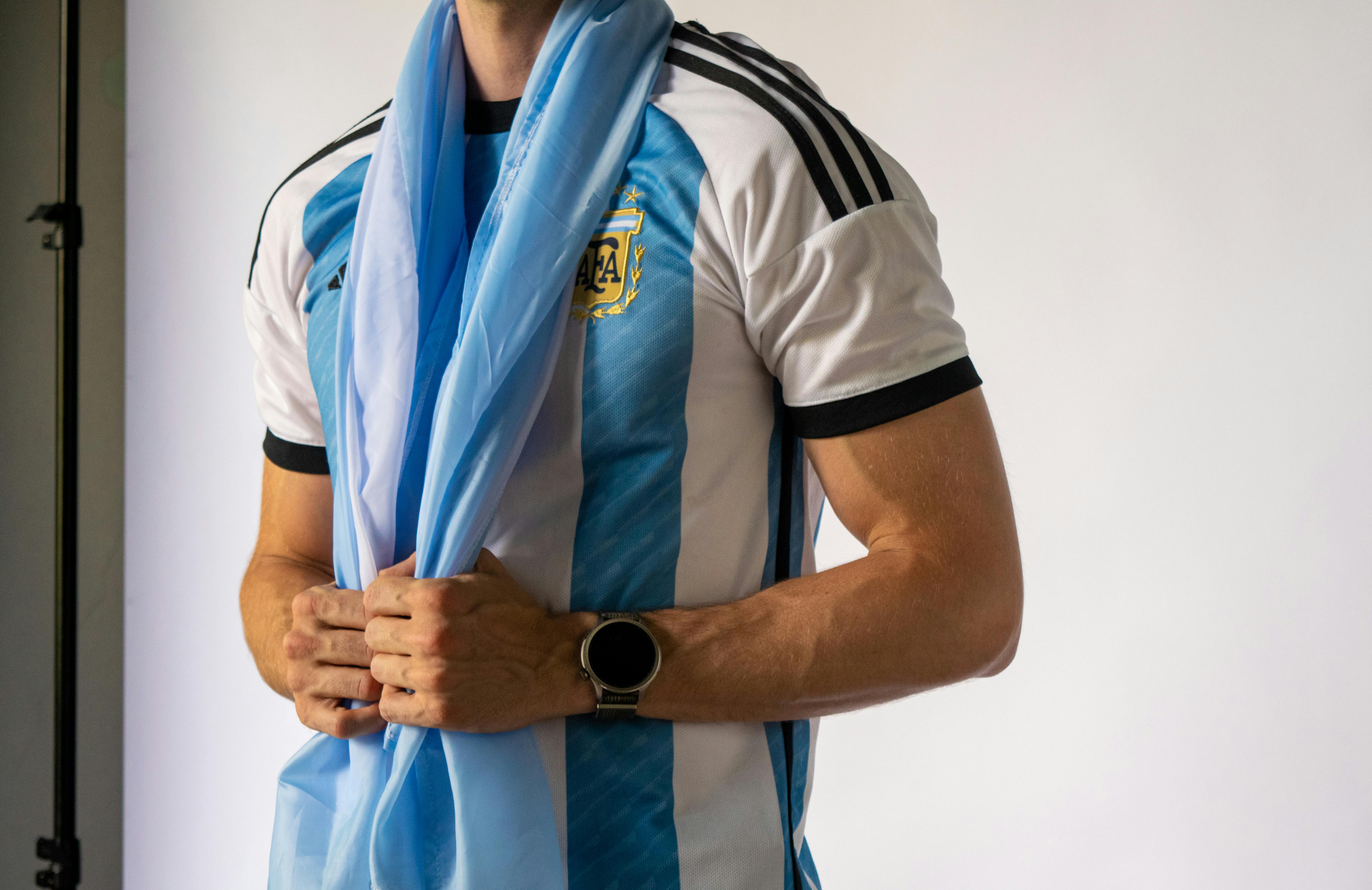 Close-up of a person wearing an Argentina jersey holding a flag, indoors.