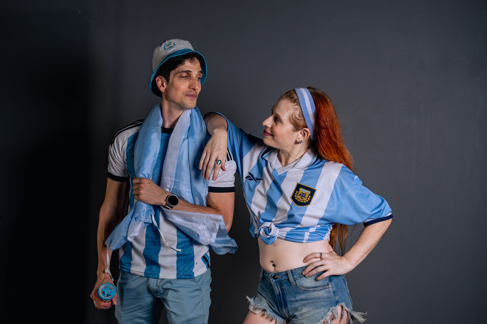 Two enthusiastic Argentinian soccer fans in team jerseys celebrating a victory indoors.