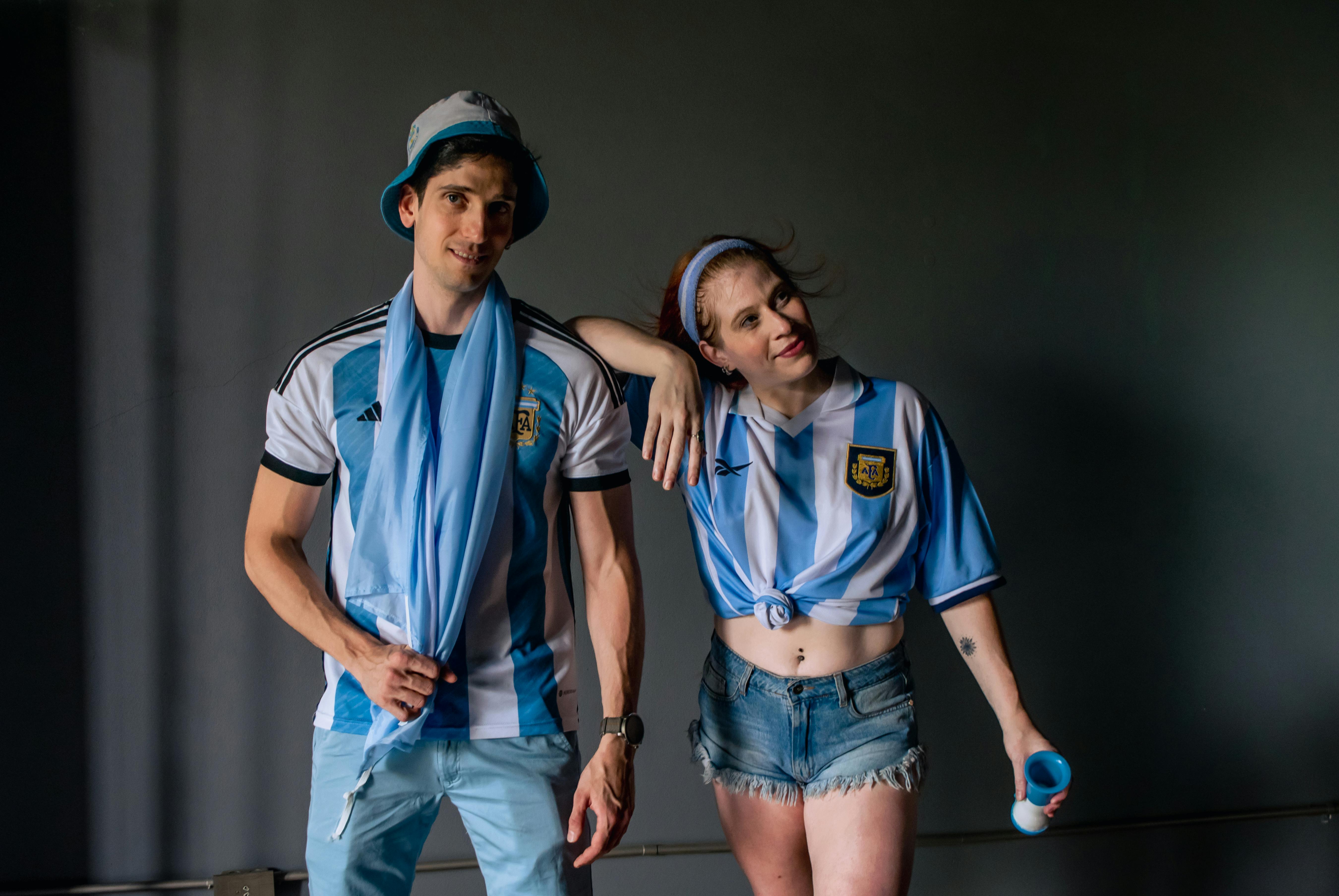 ingyenes Két argentin focimezben lévő felnőtt pózol egy laza beltéri fotón, csapatszellemet demonstrálva. Stockfotó