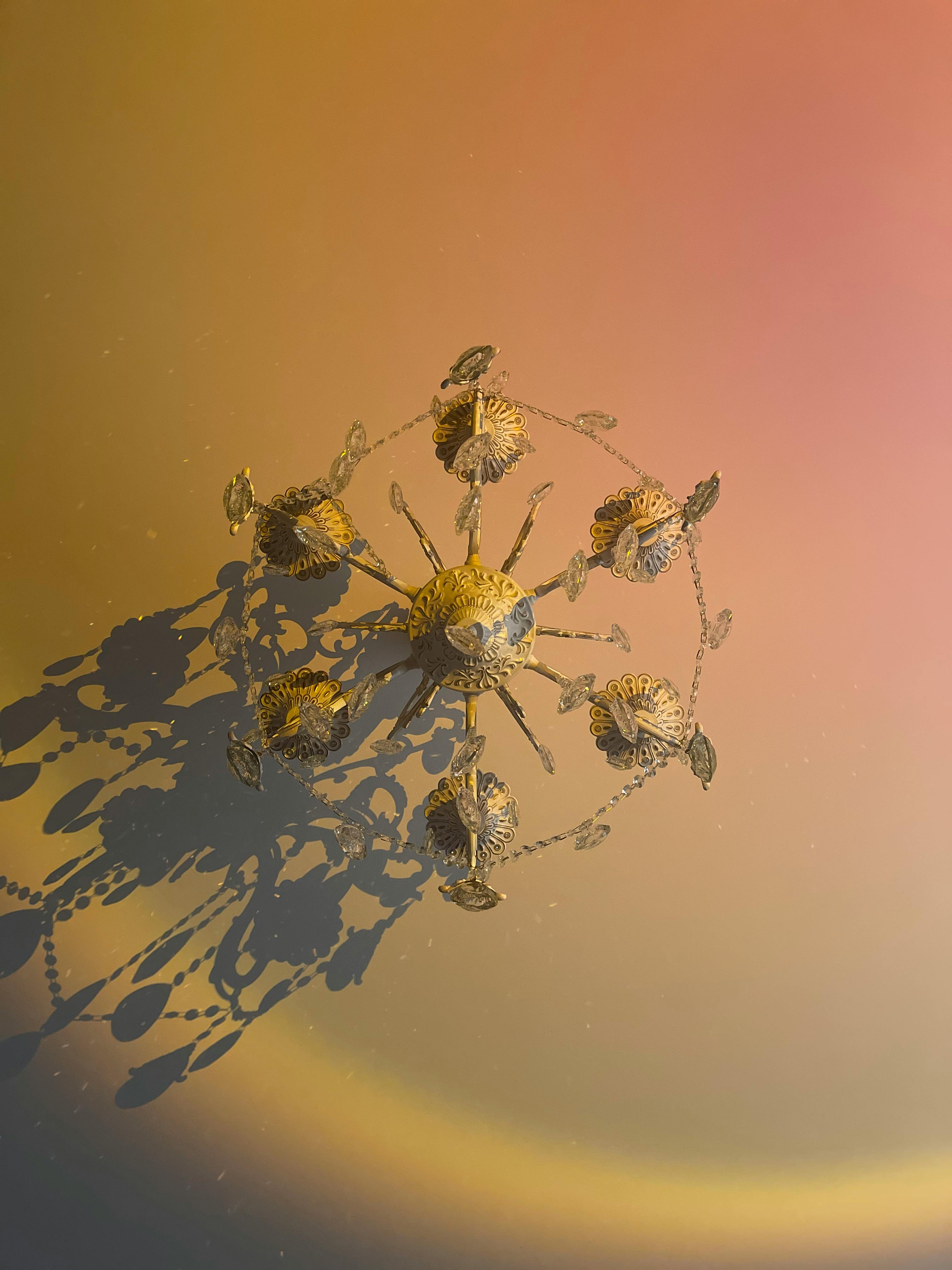 Gratis Una lámpara de araña vintage que proyecta sombras intrincadas sobre un fondo degradado cálido. Foto de stock