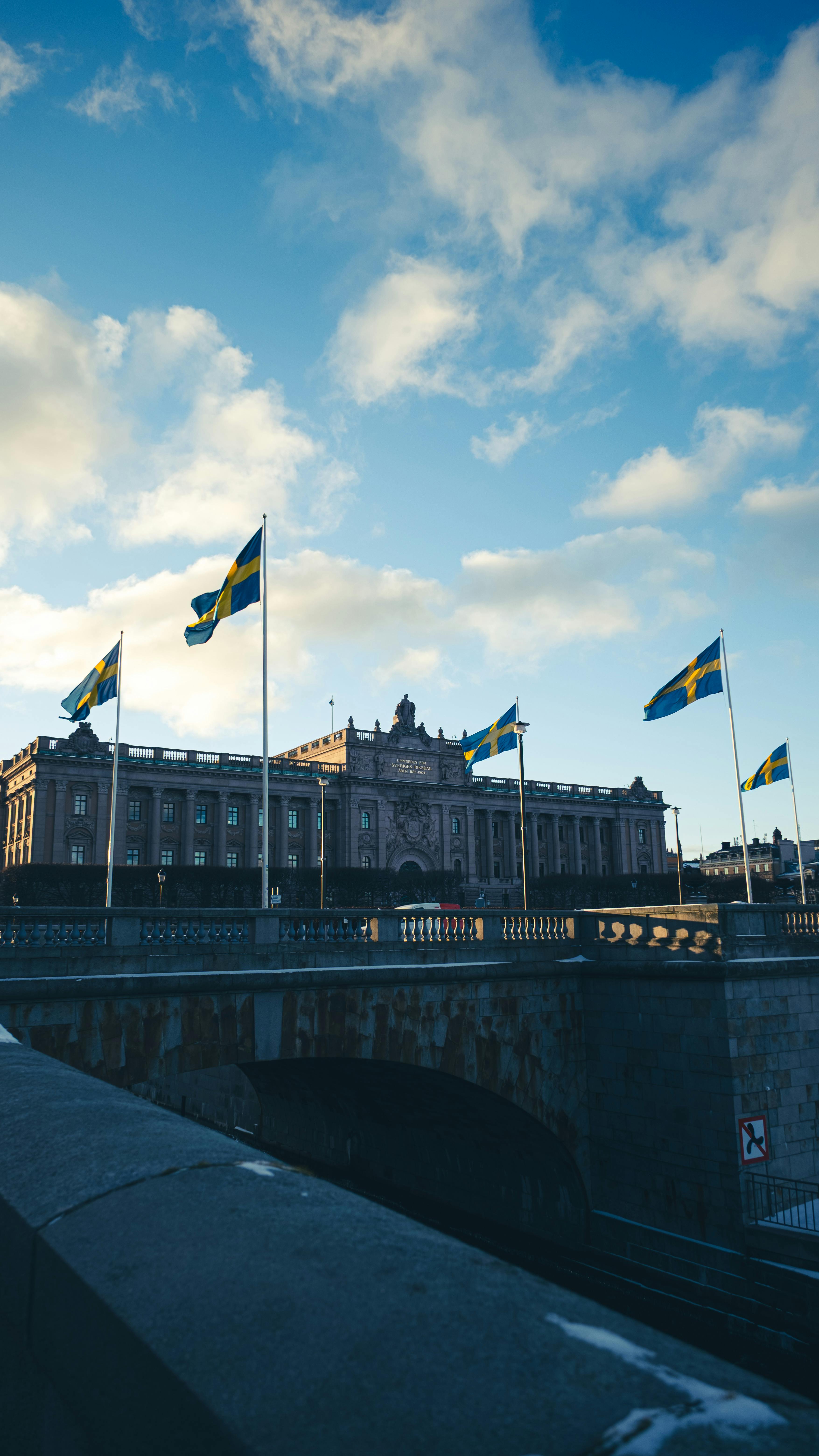 Gratis Den svenske riksdagsbygningen i Stockholm med flagg som vaier under en klar blå himmel. Arkivbilde