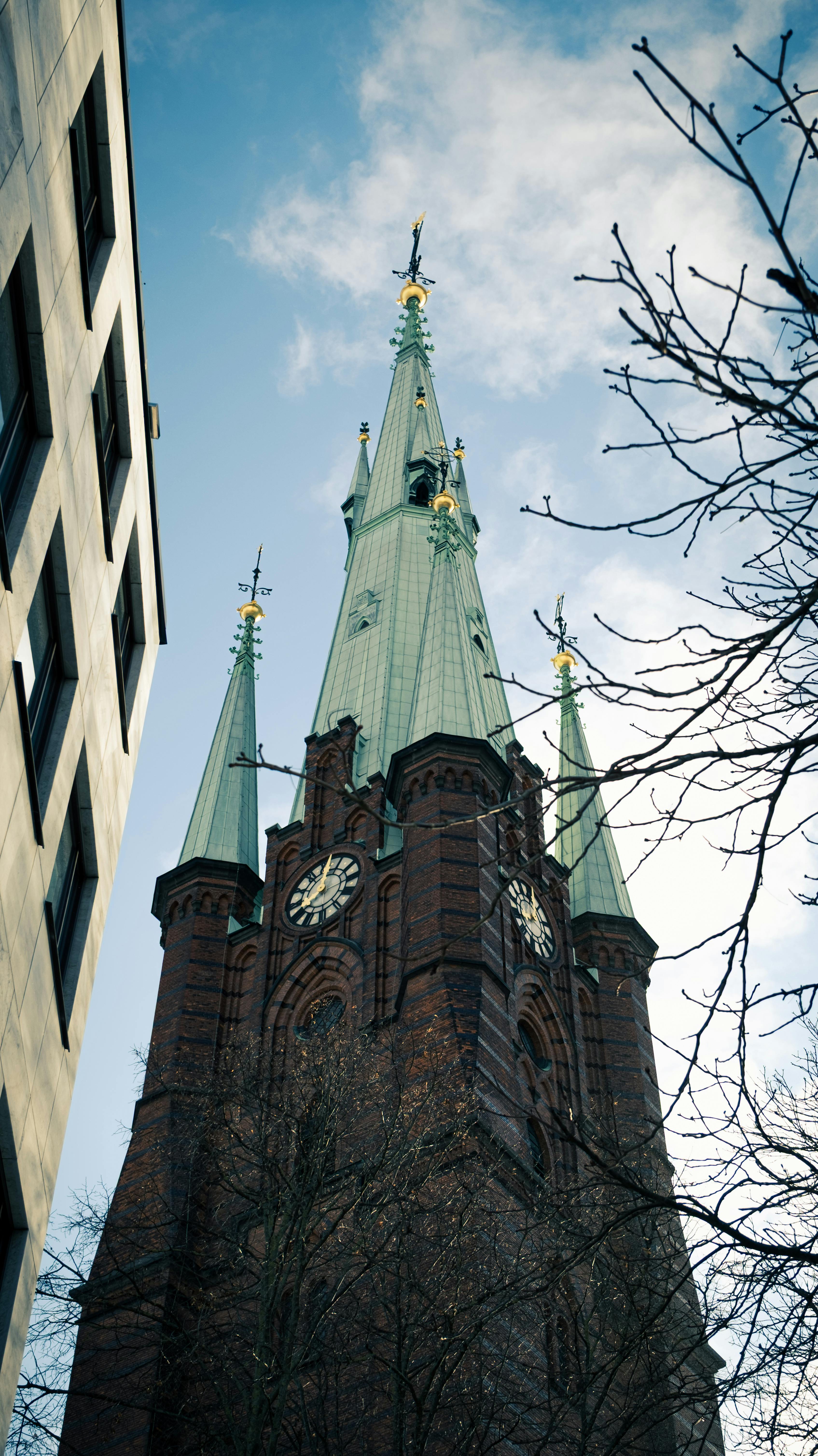 Gratis Utsikt oppover mot spirene og klokken i Sankt Johannes kirke i Stockholm mot en klar blå himmel. Arkivbilde
