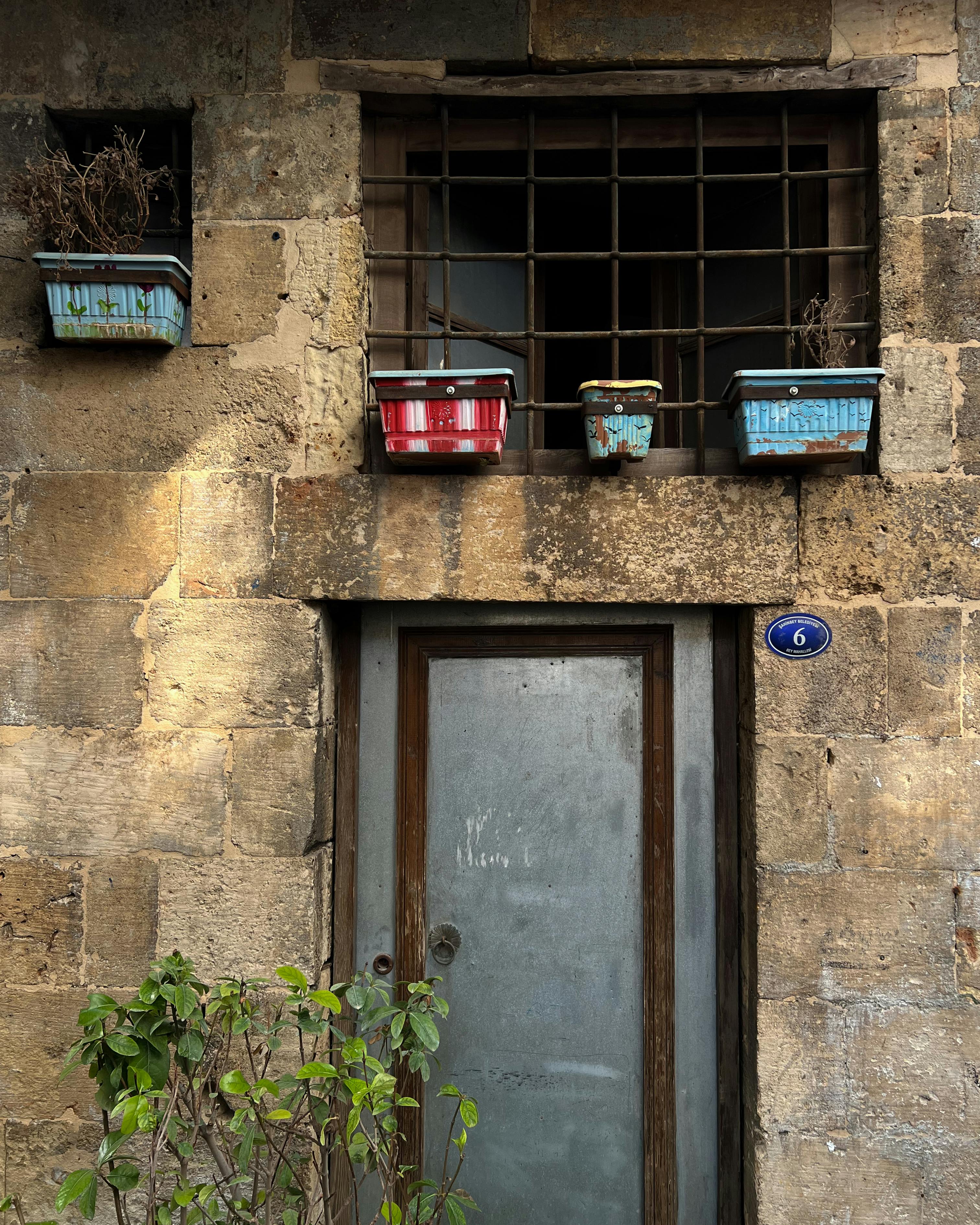 Kostnadsfria Väderbiten stenmur med dörr och krukväxter, utomhusstadsmiljö. Stock foto