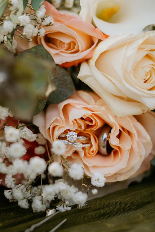 Free Close-up of wedding rings nestled in a bouquet of peach roses and delicate flowers. Stock Photo