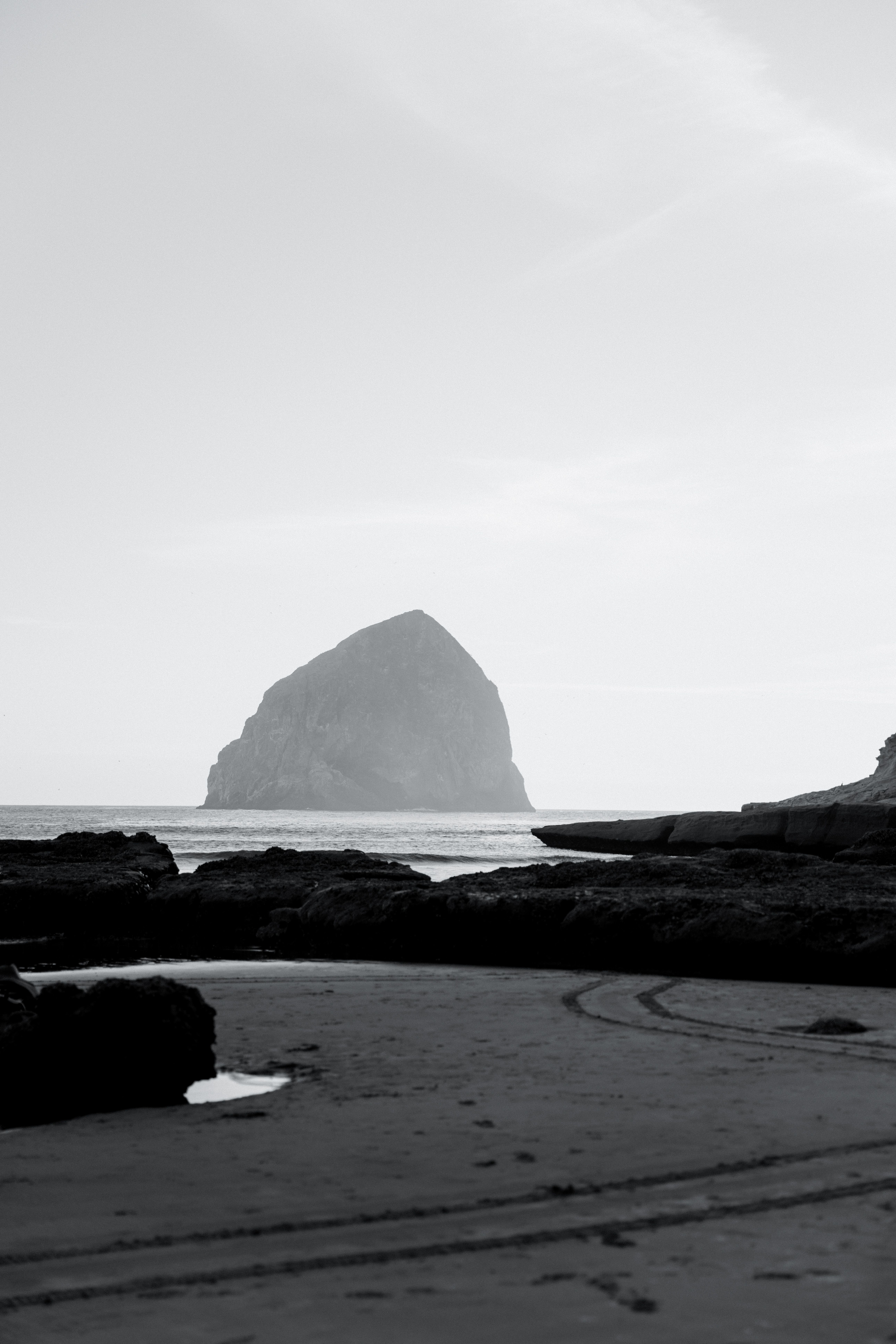 Black and white coastal view showcasing Haystack Rock with serene ocean and beach.