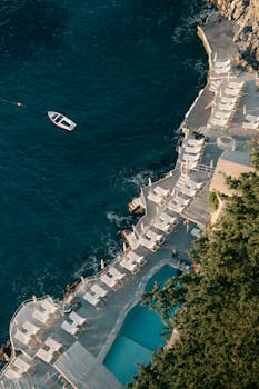 Aerial shot of a coastal resort with lounging area and small boat in the ocean.