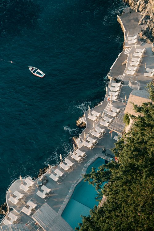Free Aerial shot of a coastal resort with lounging area and small boat in the ocean. Stock Photo