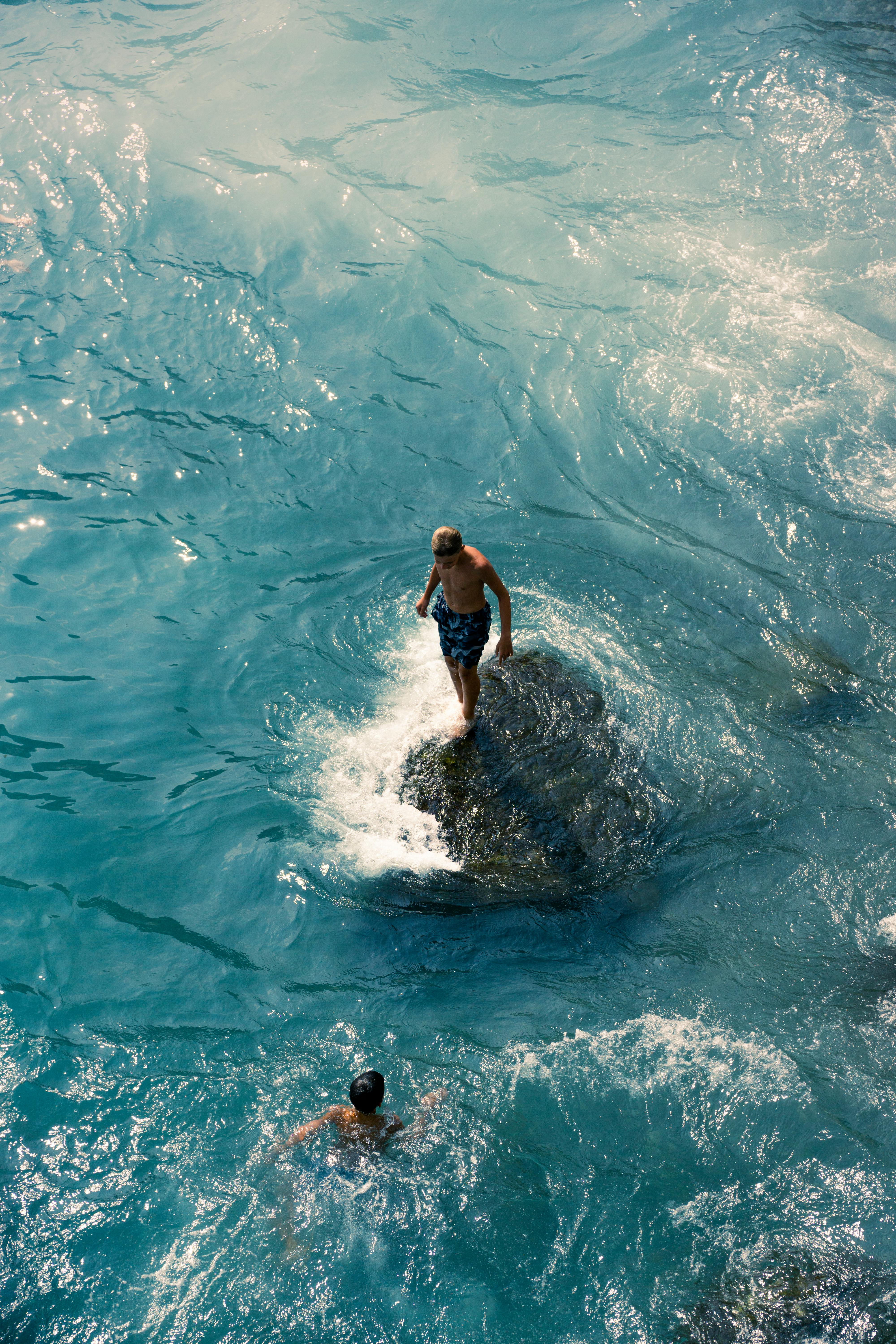 Two men enjoy swimming and climbing rocks in the vibrant ocean, embracing adventure and nature.