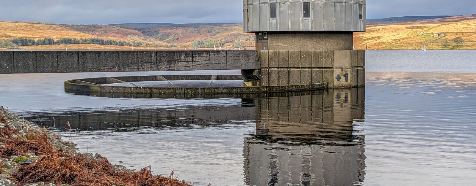 A concrete water tower reflecting in a serene lake amidst the English countryside.