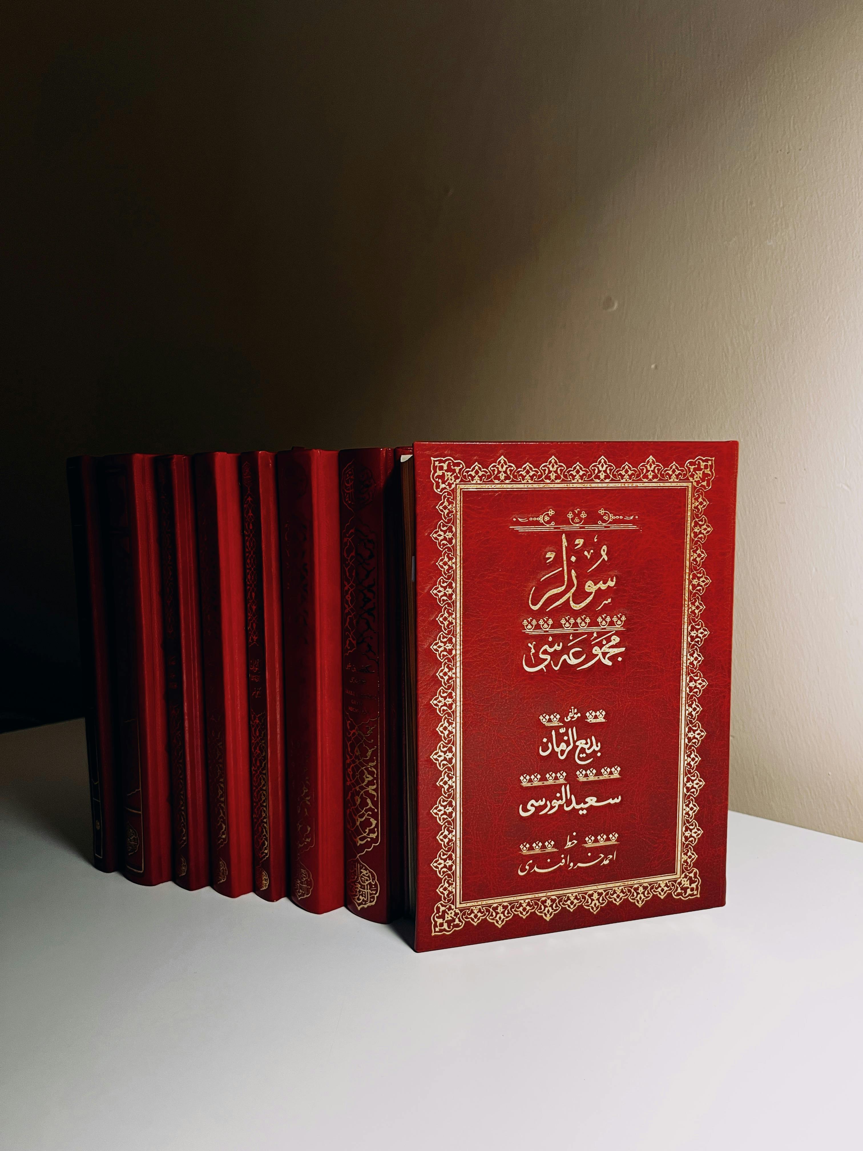 A stack of red books with intricate gold Arabic calligraphy on a plain indoor shelf.