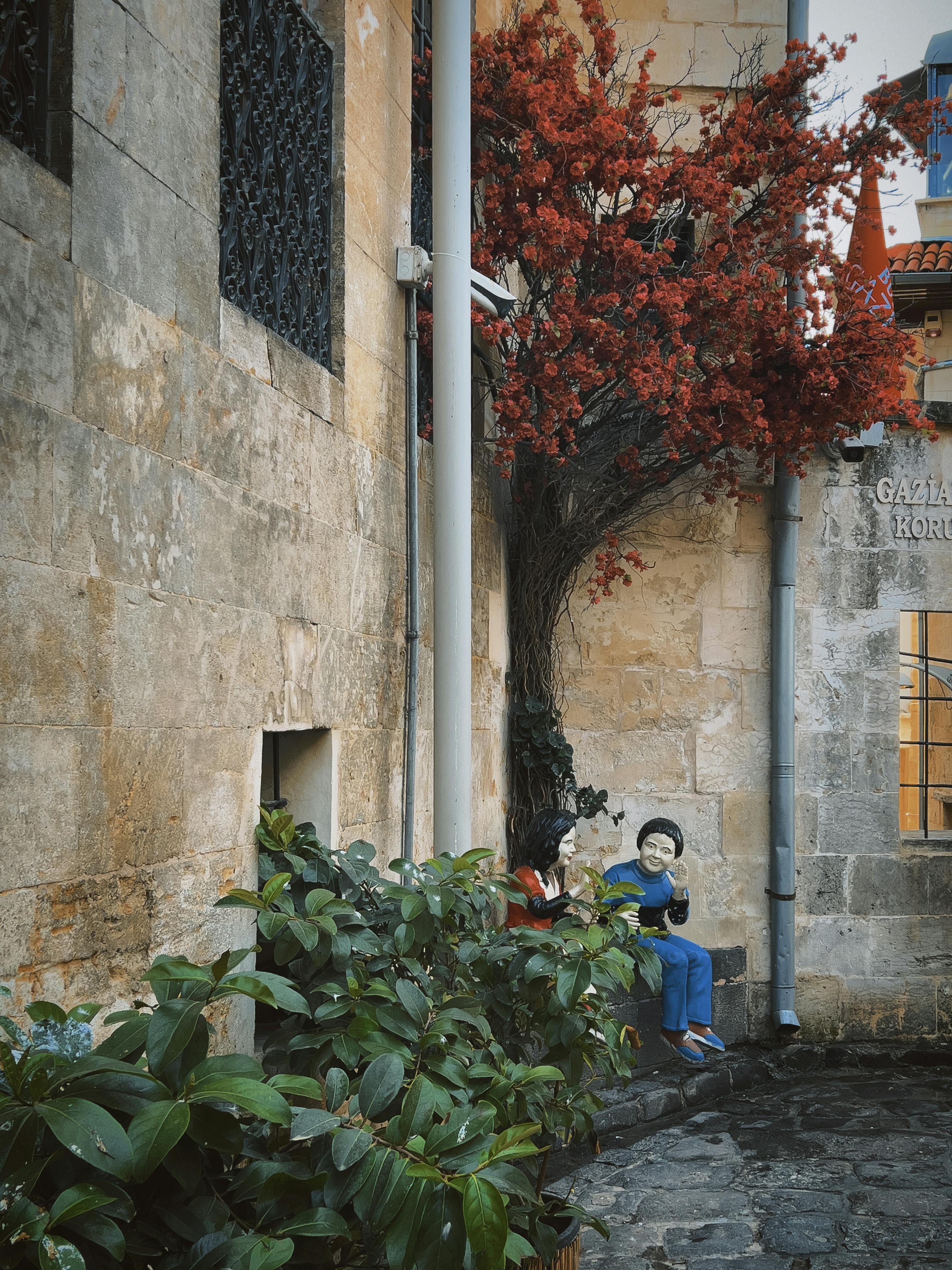 Безкоштовне Чарівна кам'яна алея з манекенами під яскраво-червоним листям, що створює химерний міський пейзаж. стокове фото