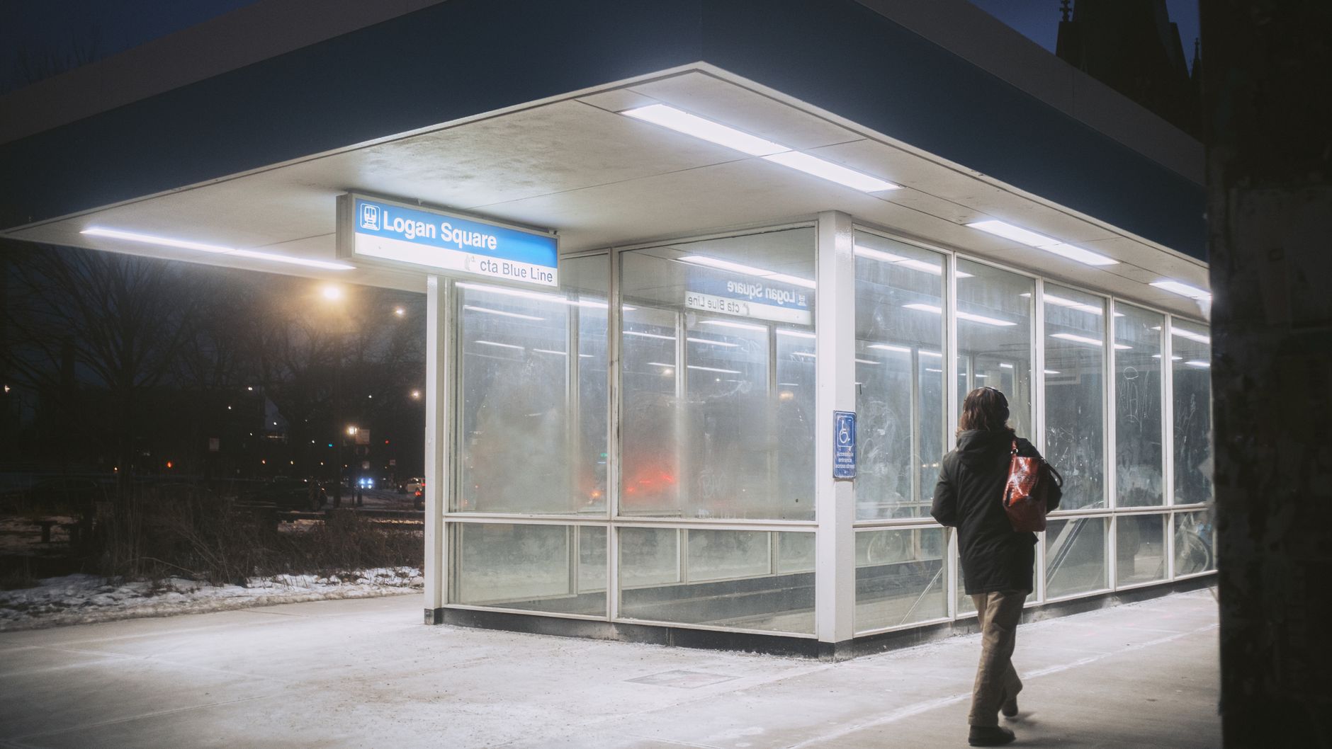 Person entering Logan Square CTA Blue Line station at night in winter.