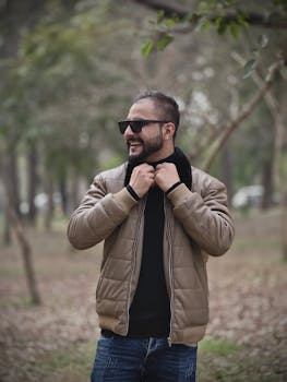 Casual portrait of a man wearing a jacket and sunglasses in a park setting.