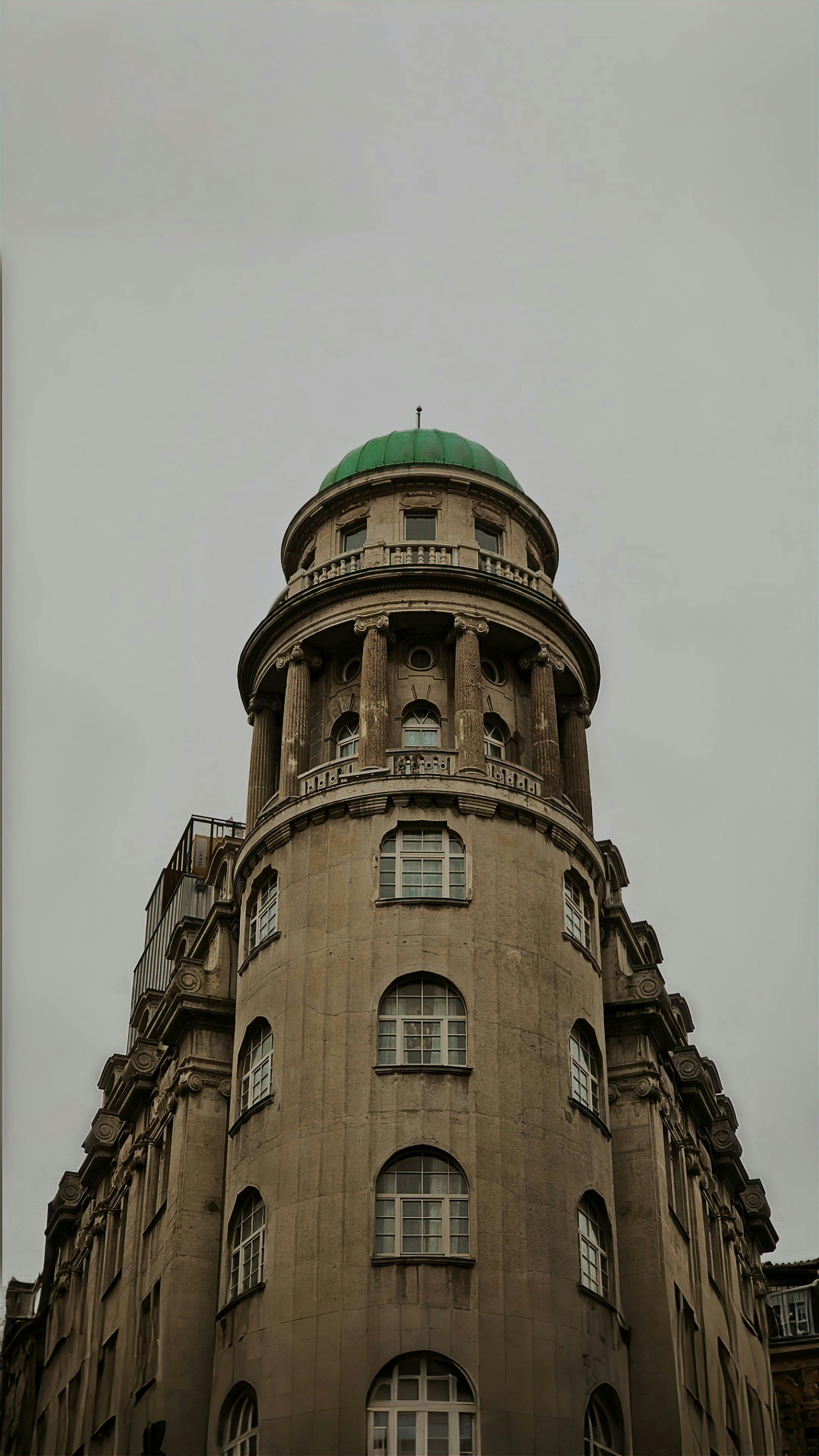 Gratis Bangunan batu tinggi dengan kubah hijau di puncaknya, dilihat dari bawah dengan latar langit berawan. Foto Stok