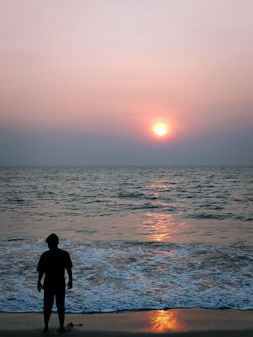 Free A serene sunset scene with a silhouette standing on the beach by the ocean. Stock Photo