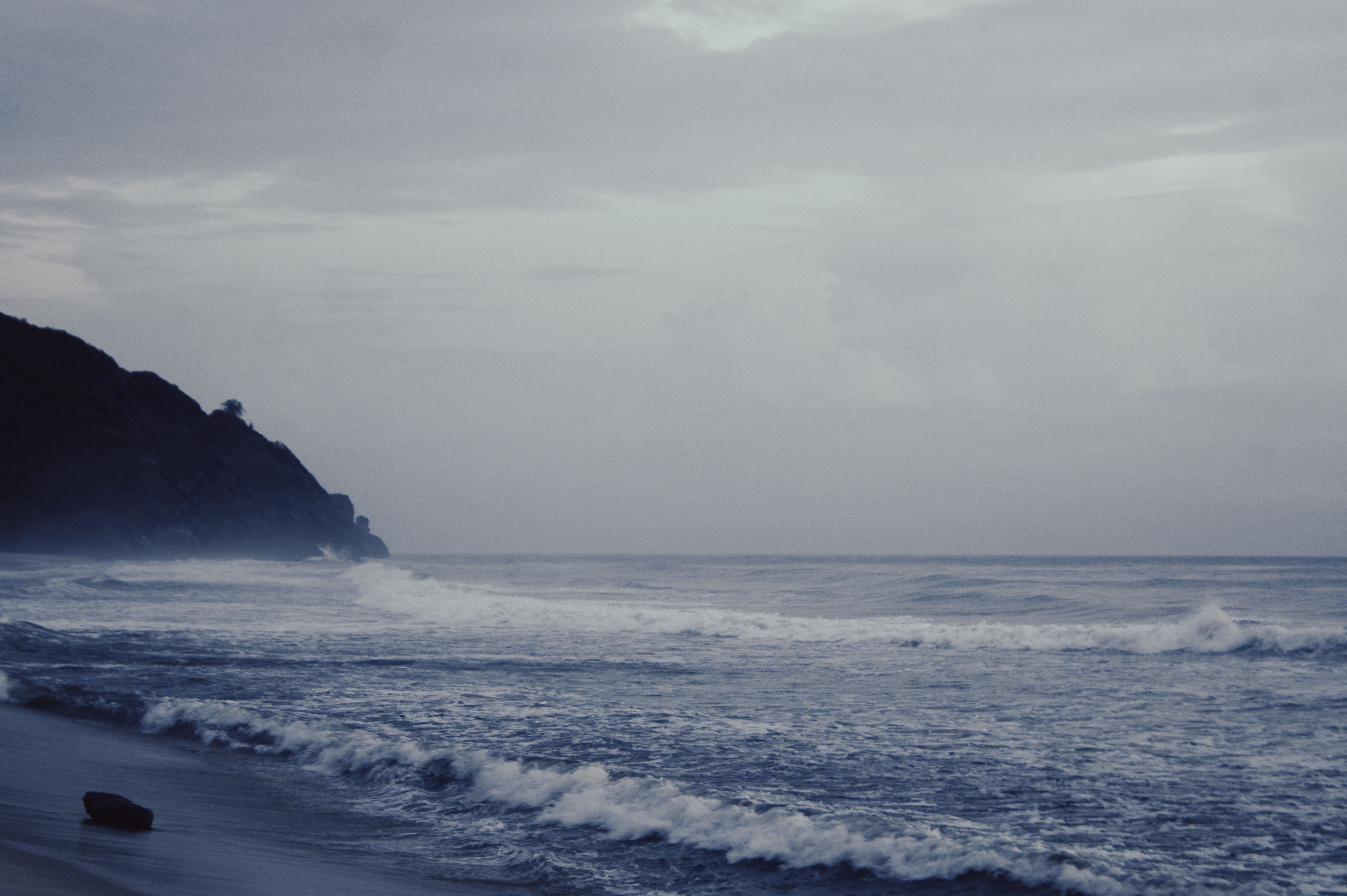 Serene waves lapping at a rocky coastline captured on a misty day, evoking peace and solitude.