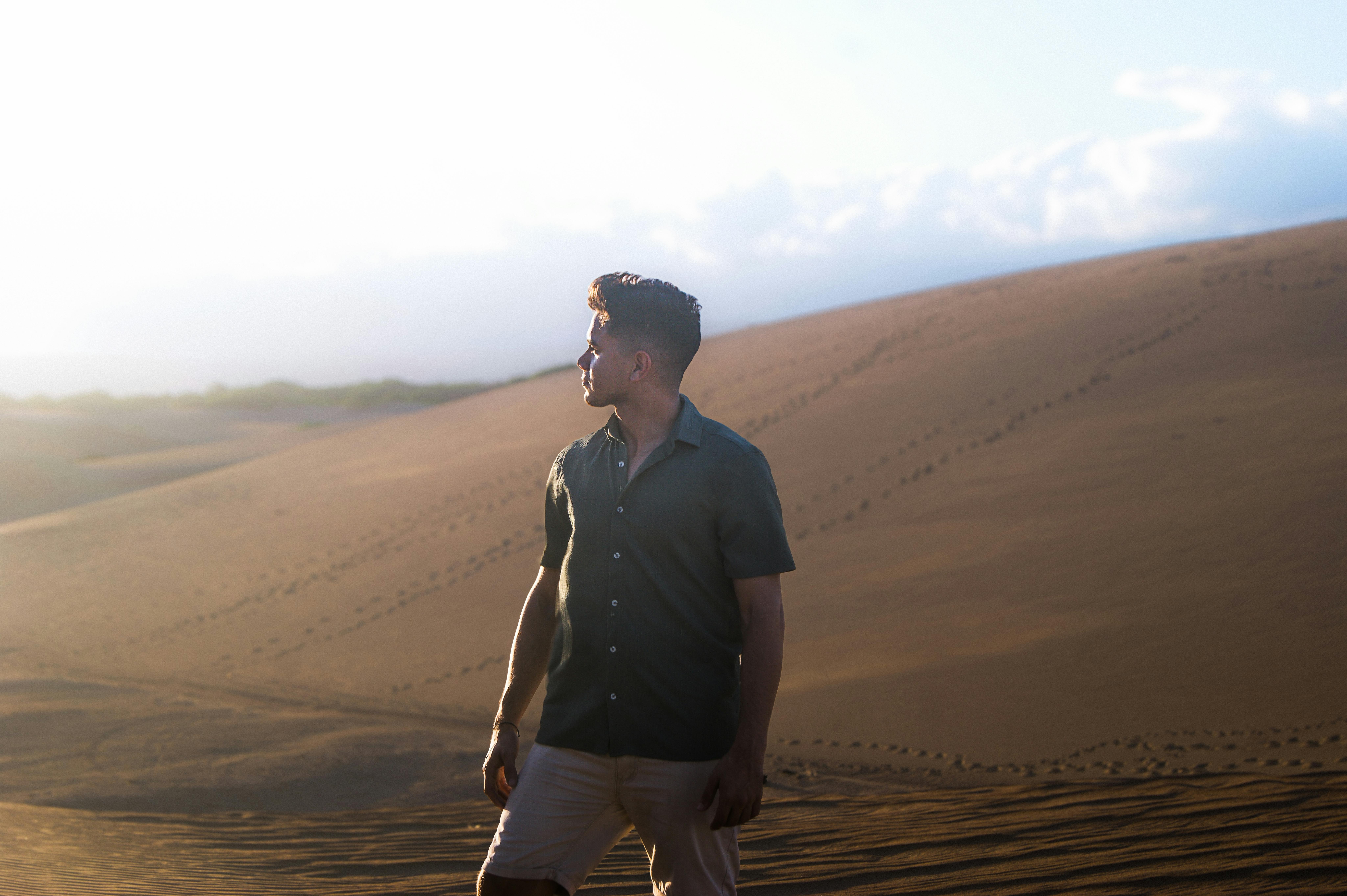 ingyenes Egy férfi a távolba néz, egy hatalmas homokdűnén áll napfelkeltekor. Stockfotó