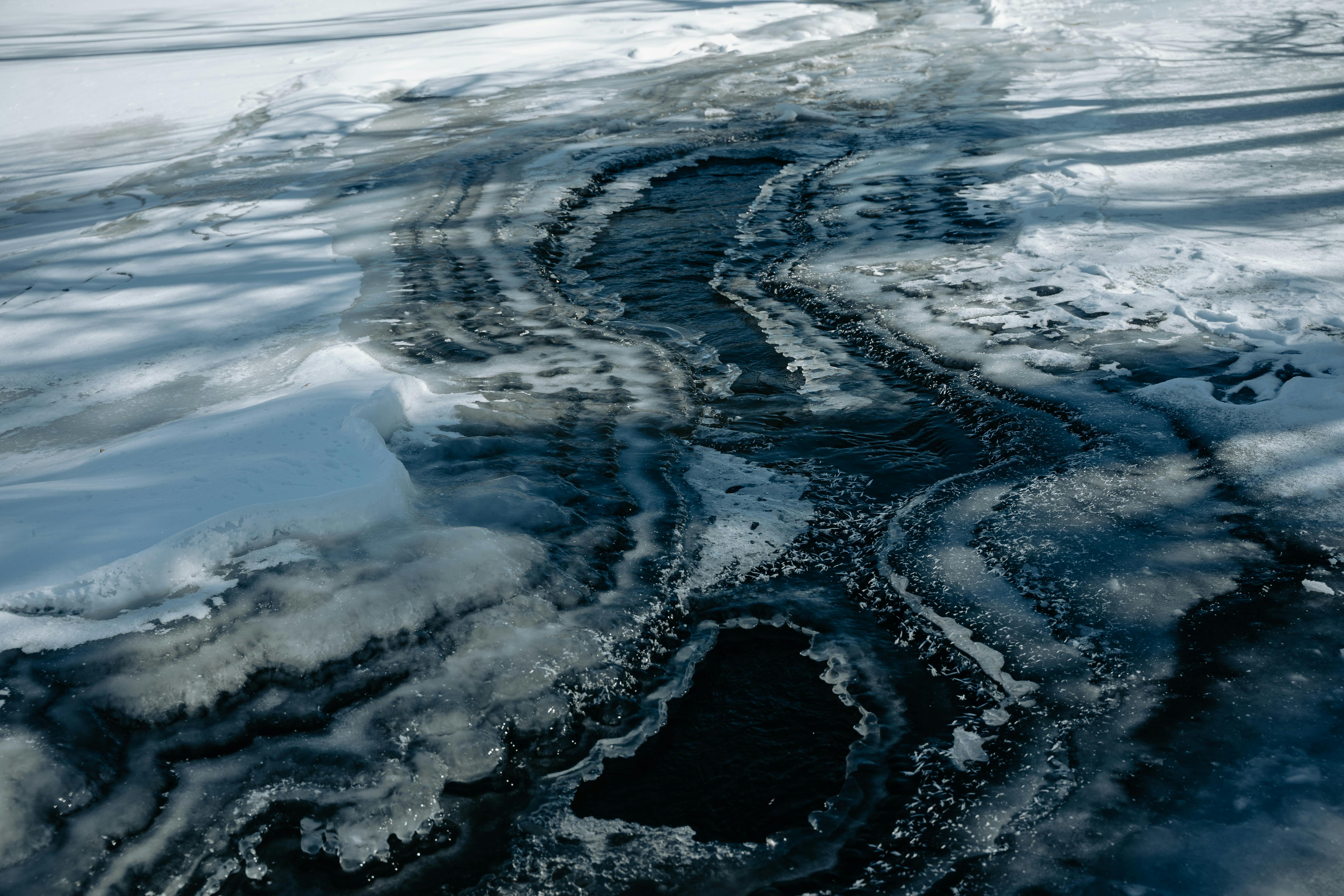 無料 冬の間に撮影された、印象的な氷の溶ける模様を持つ凍った川の抽象的な空中写真。 写真素材