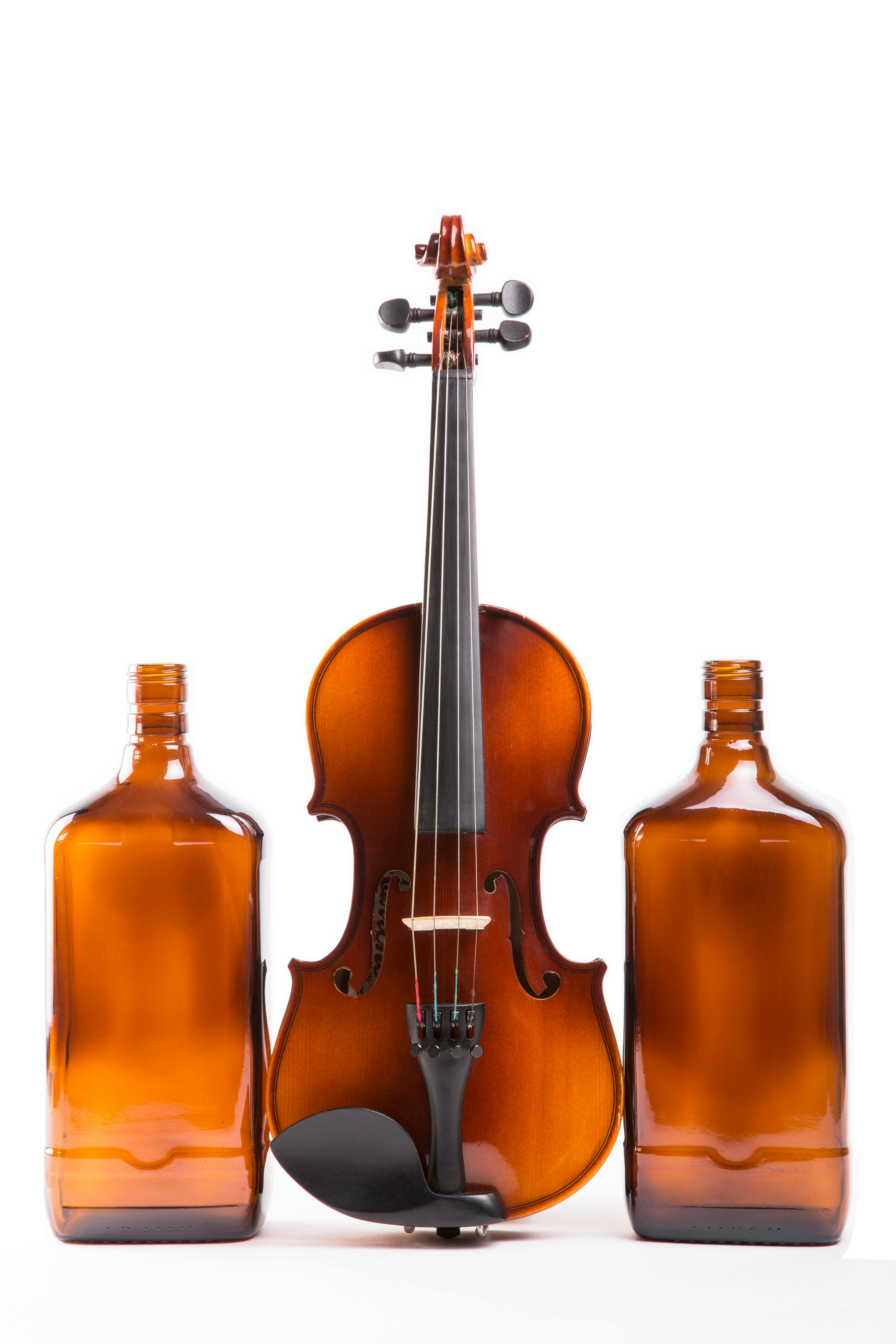Studio shot of a violin flanked by two amber bottles on a white background.
