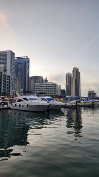 Sunset view of yachts docked at Dubai Marina with skyscrapers reflecting on the water.