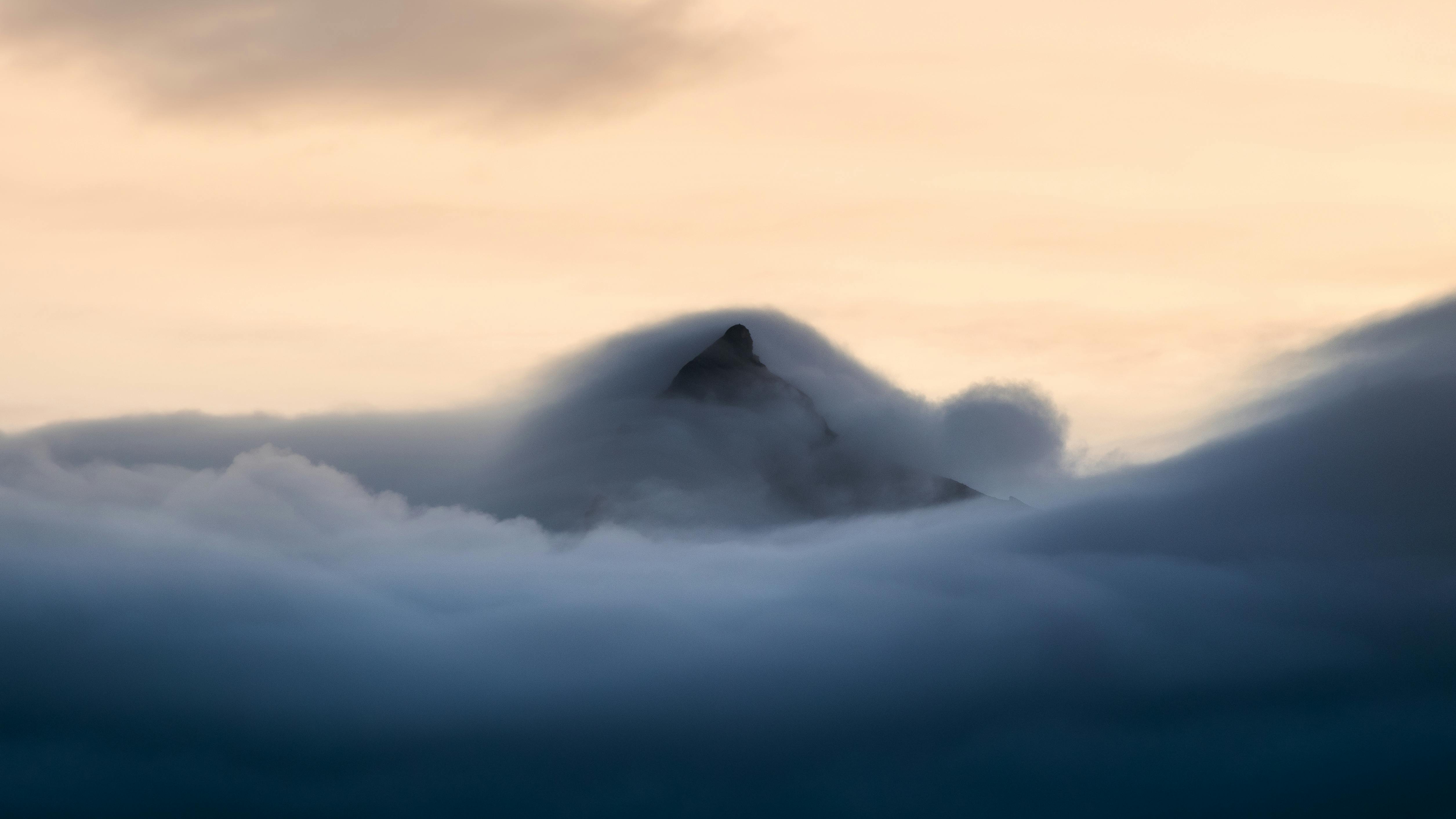 Gratis En fantastisk utsikt over en fjelltopp som trenger gjennom skyene ved solnedgang og skaper en drømmende atmosfære. Arkivbilde