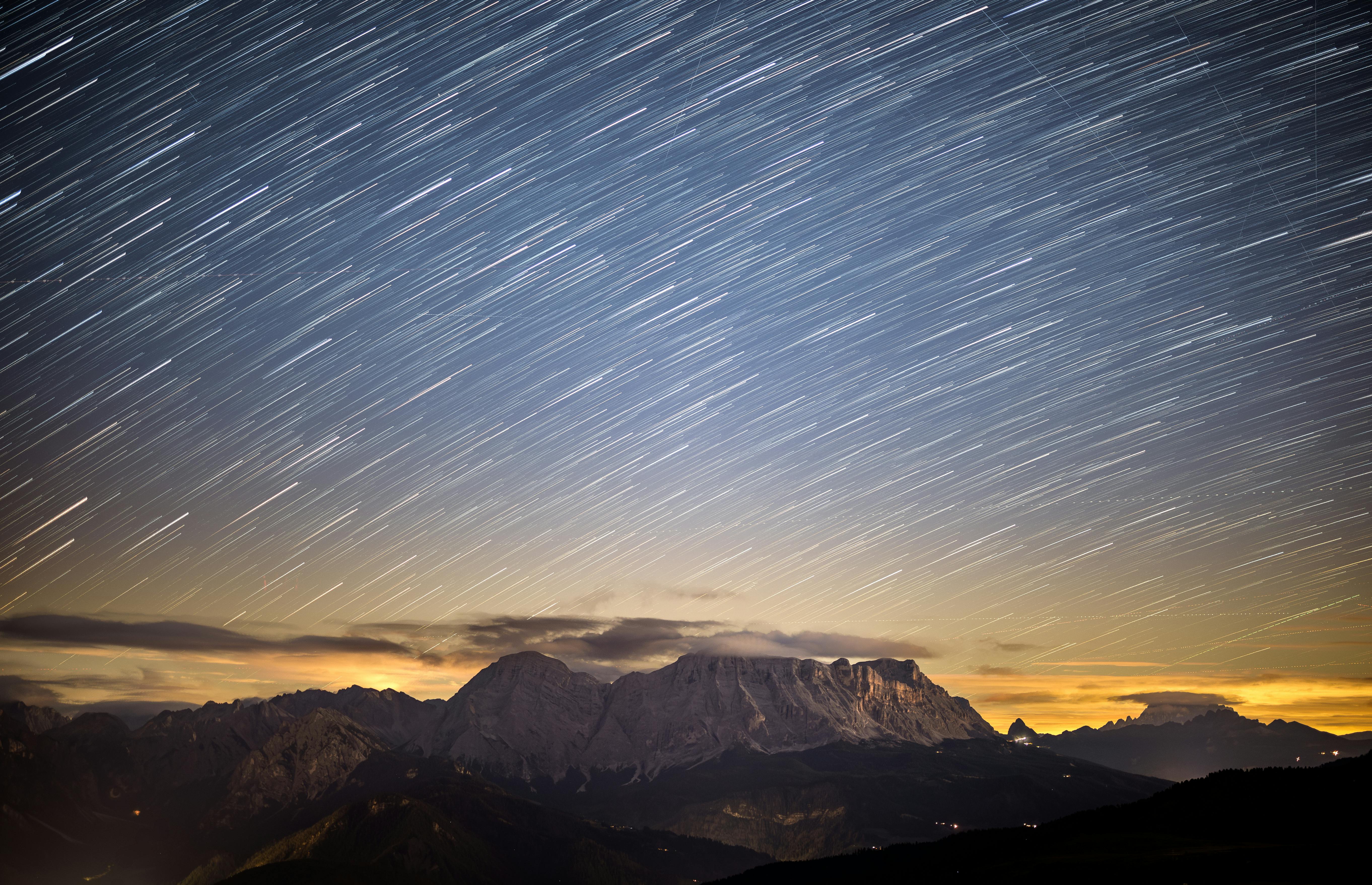 Dramatic long exposure of star trails above the Dolomite mountains at sunset, showcasing a stunning natural landscape.