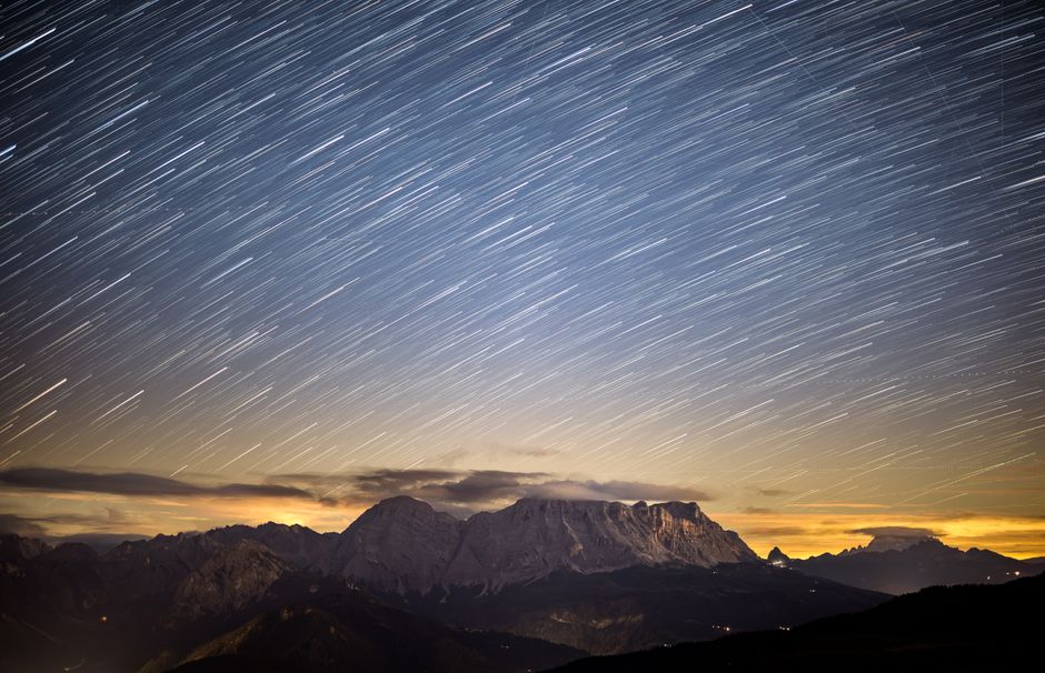 Dramatic long exposure of star trails above the Dolomite mountains at sunset, showcasing a stunning natural landscape.