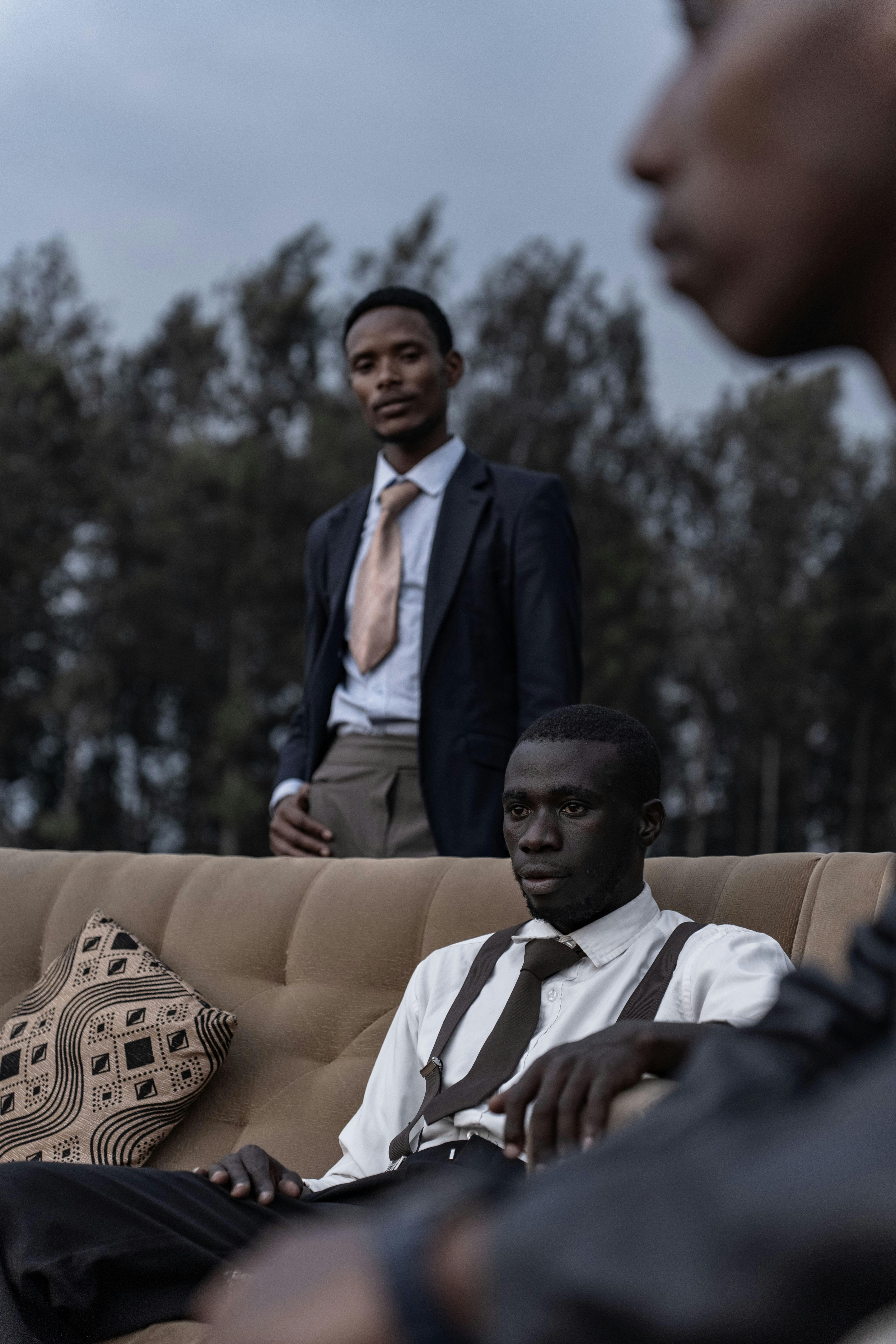 бесплатная Стильные темнокожие мужчины в костюмах позируют на диване на открытом воздухе, создавая современный модный портрет. Стоковое фото