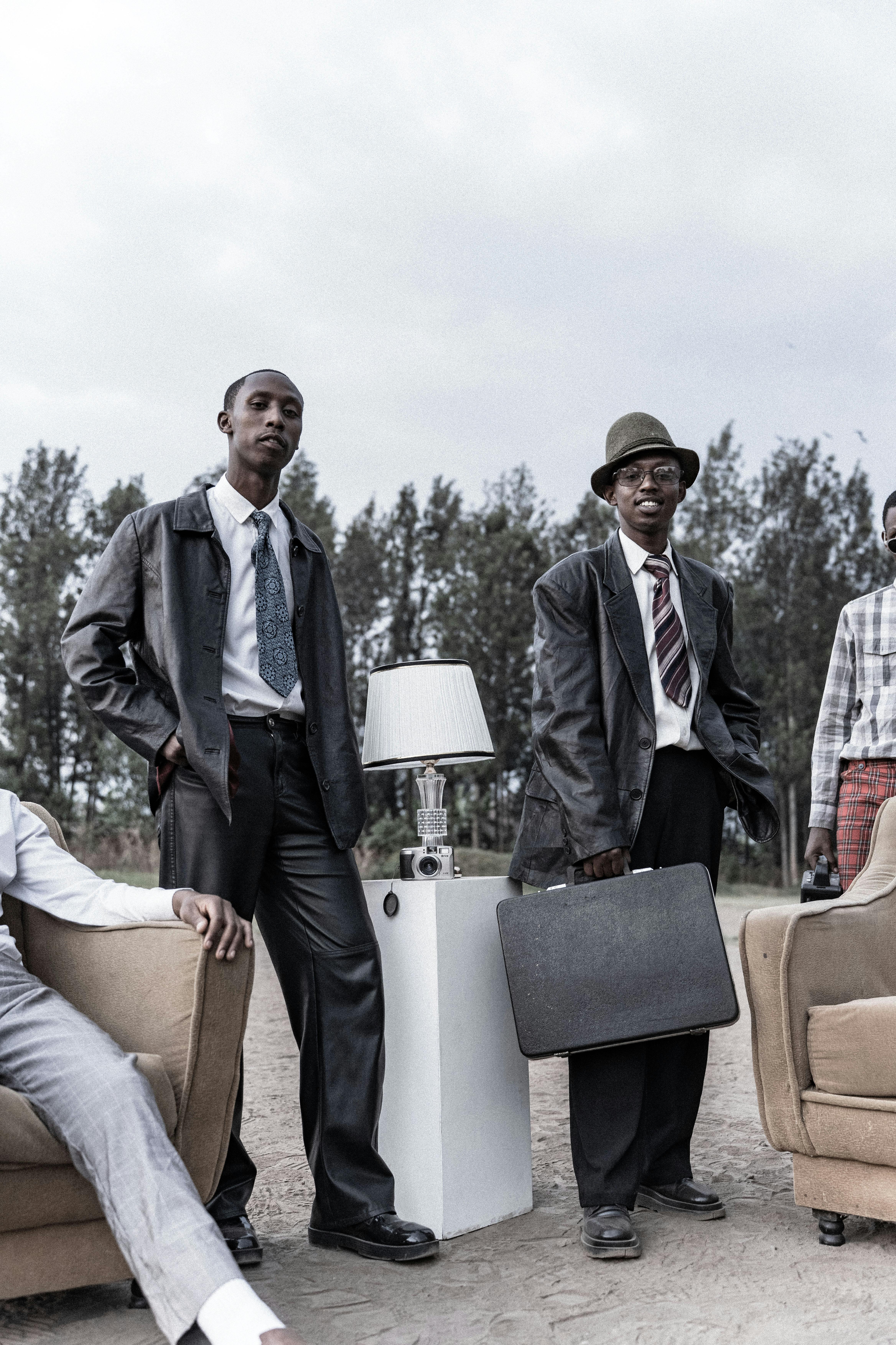 бесплатная Стильные мужчины в костюмах в стиле ретро позируют на открытом воздухе с винтажными аксессуарами под облачным небом. Стоковое фото