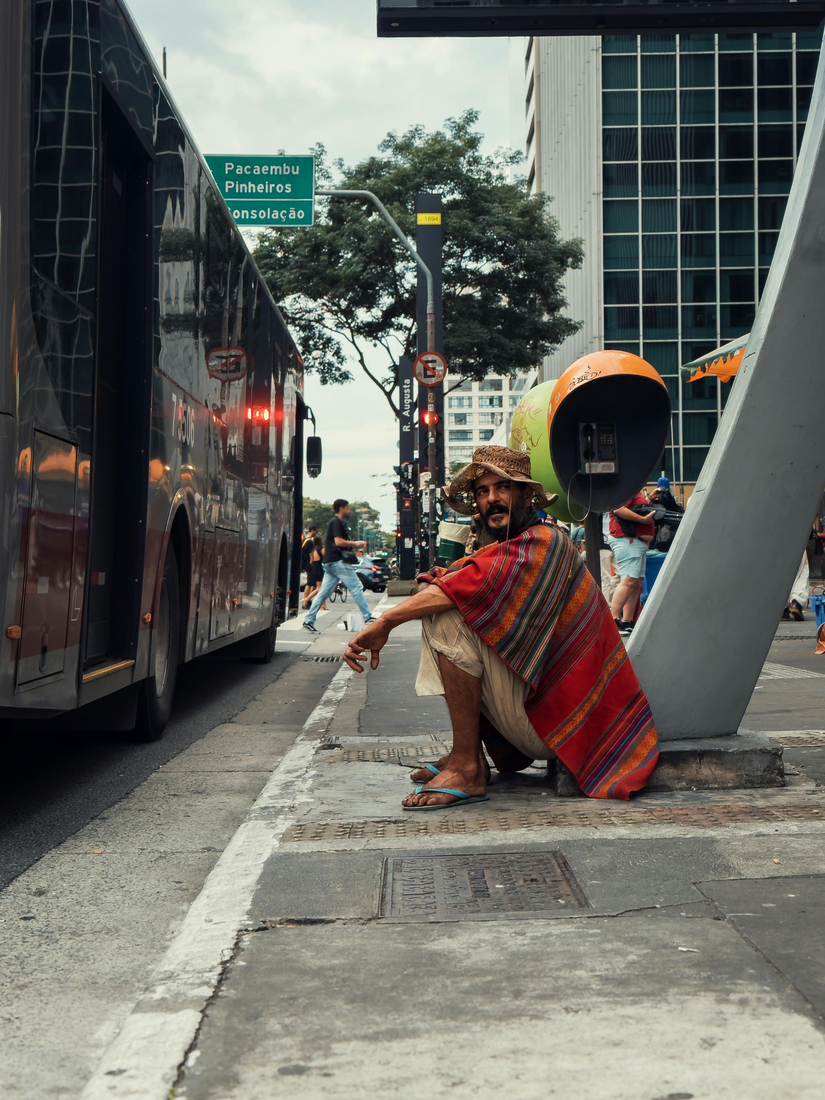 免费 一名身穿色彩鲜艳的披风的男子坐在圣保罗街头，展现出充满活力的都市景象。 素材图片