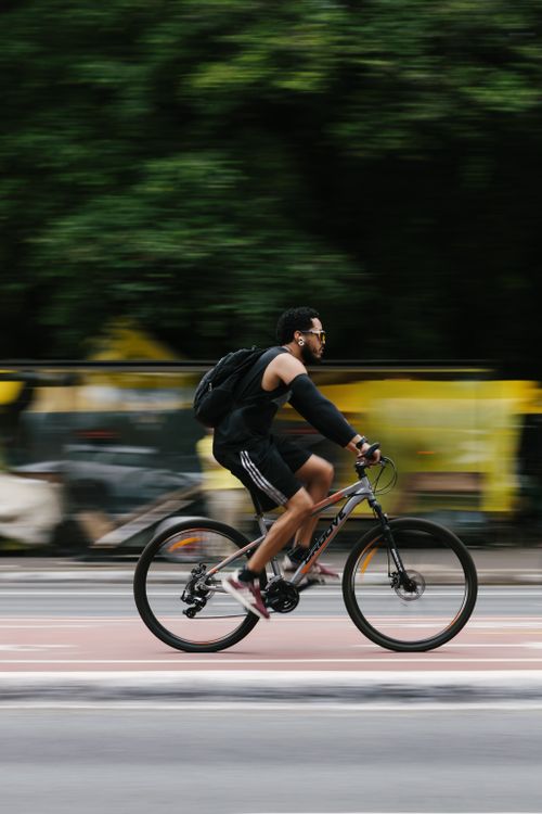 Free A man rides a bicycle swiftly along a city road, with a blurred background for motion effect. Stock Photo