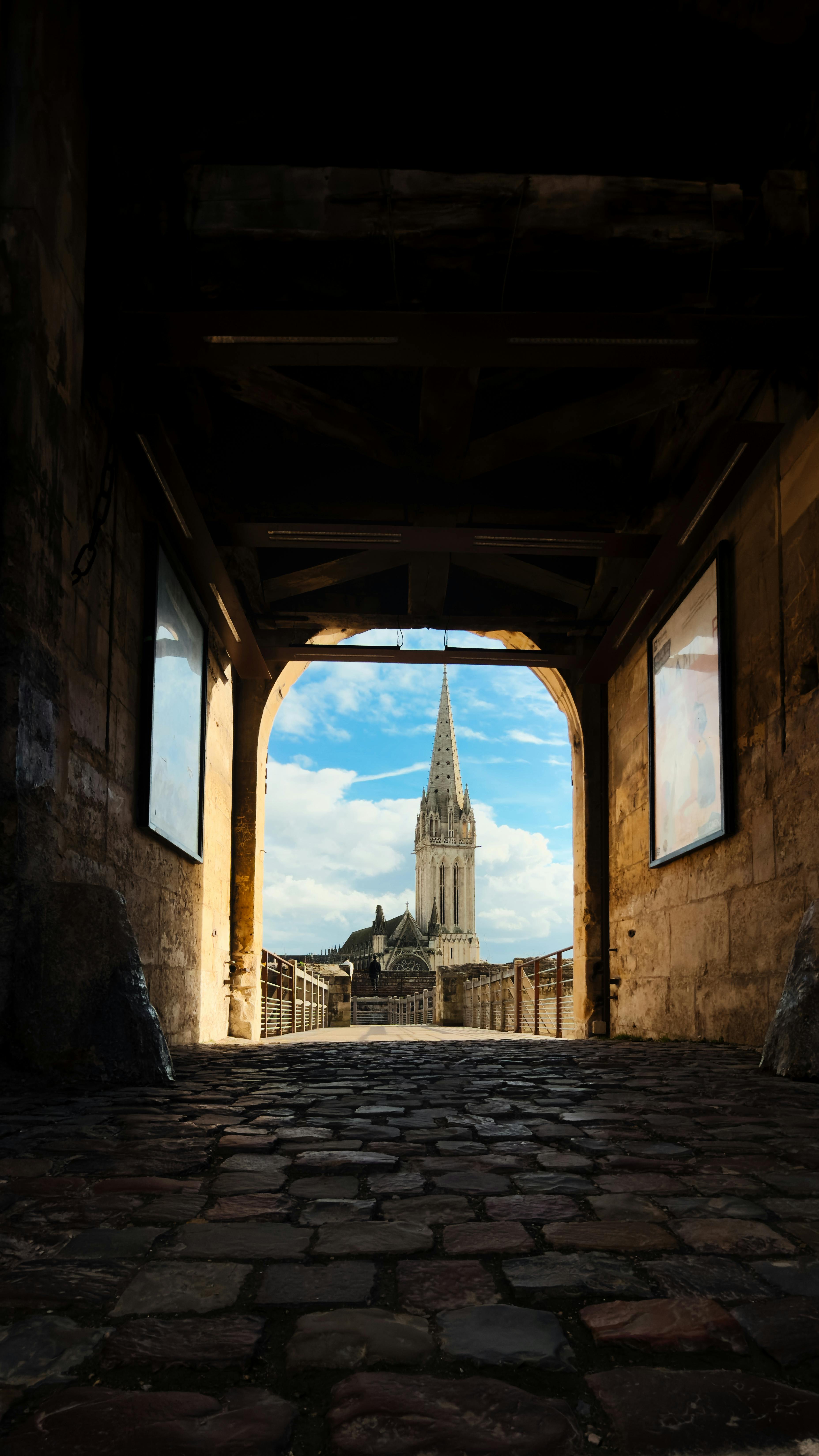 Gratis Gotisk katedralspir innrammet av en rustikk steinbue, som viser frem middelalderarkitektur. Arkivbilde