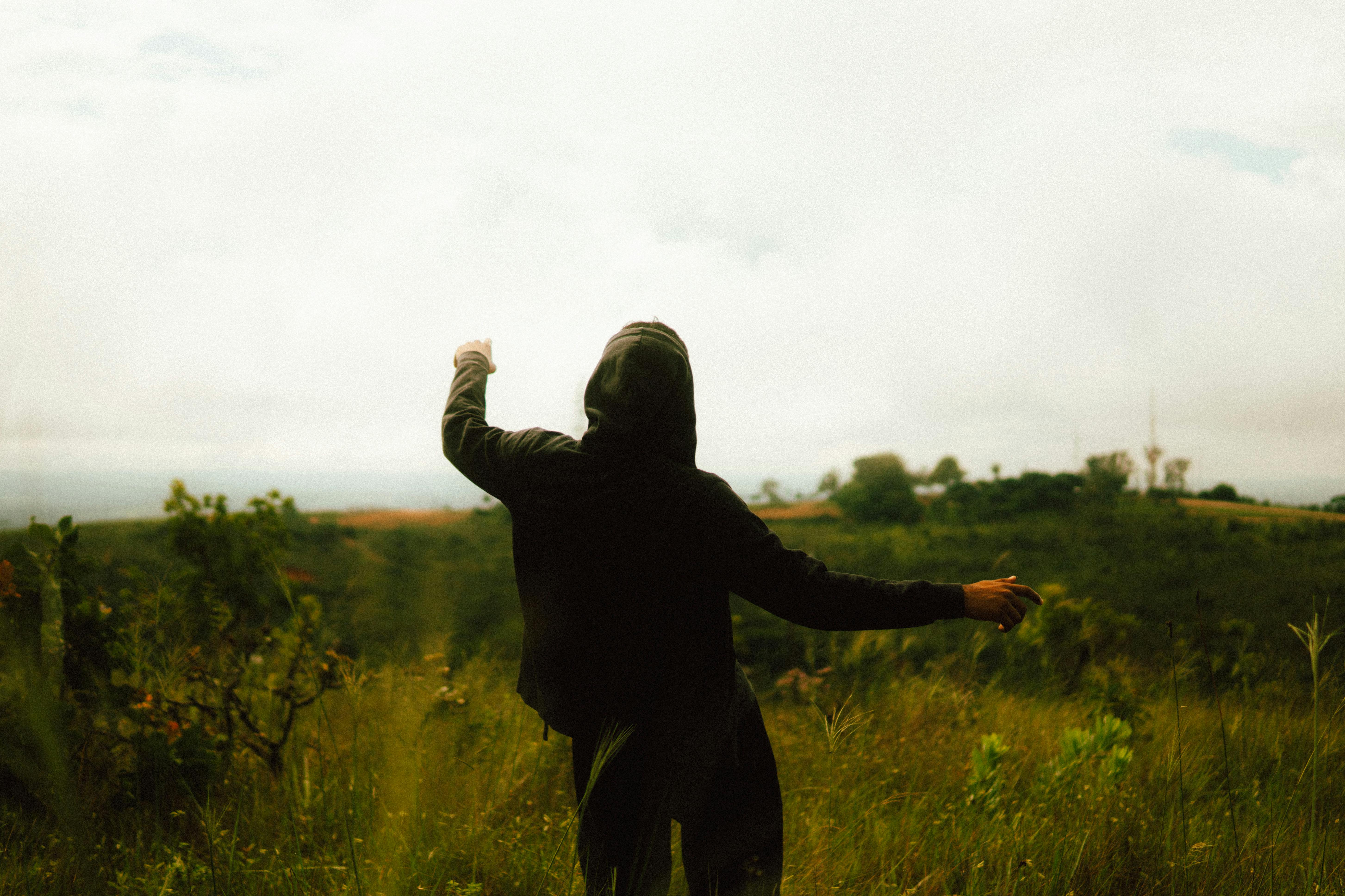 Free A person in a hoodie enjoys nature in a serene outdoor setting, surrounded by greenery. Stock Photo