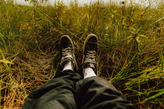 Person sitting in tall grass wearing sneakers, capturing a moment of relaxation and tranquility.