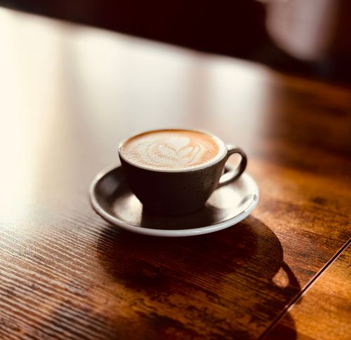 Free A beautifully crafted latte in a ceramic cup with heart-shaped latte art on a wooden table in warm lighting. Stock Photo