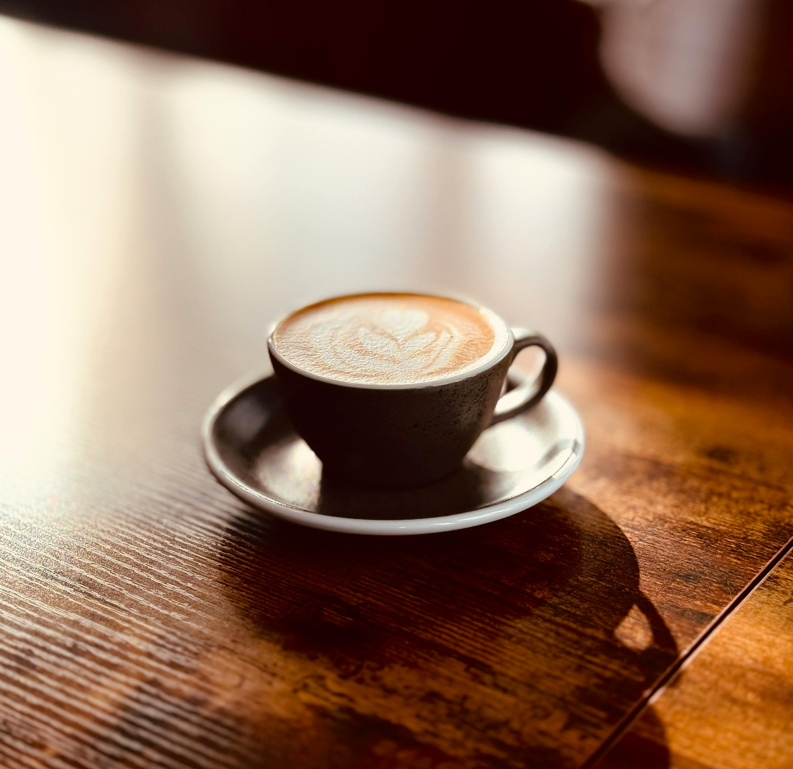 Kostnadsfria En vackert utformad latte i en keramisk kopp med hjärtformad lattekonst på ett träbord i varmt ljus. Stock foto