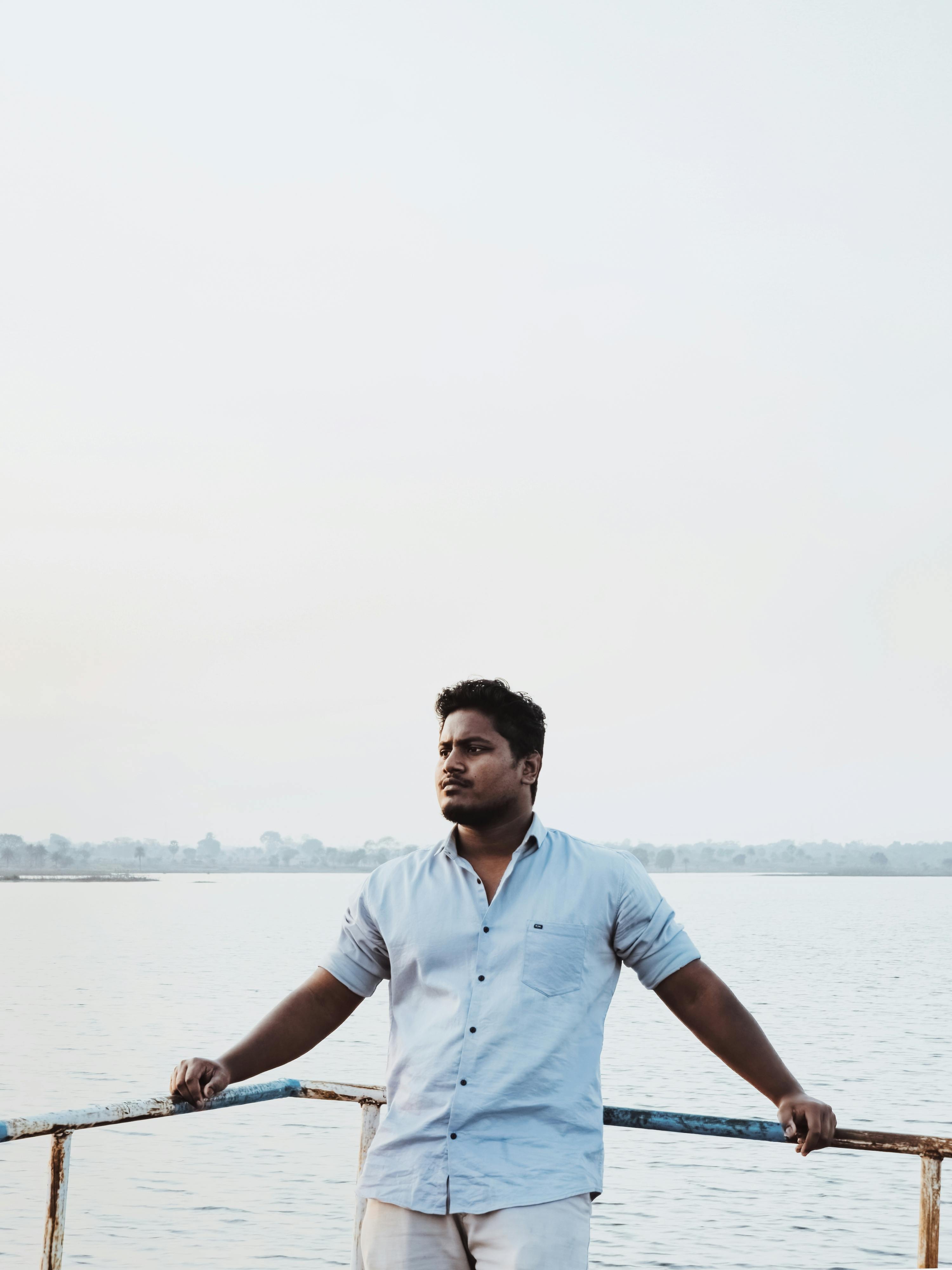 A man stands by the edge of a tranquil lake, gazing thoughtfully into the distance.