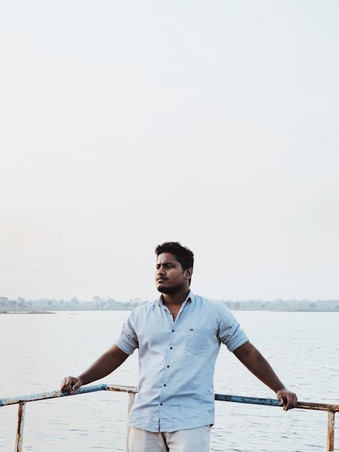 A man stands by the edge of a tranquil lake, gazing thoughtfully into the distance.