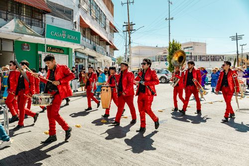 Free Musicians in vibrant red suits perform in a lively street parade in Pachuca, Mexico. Stock Photo