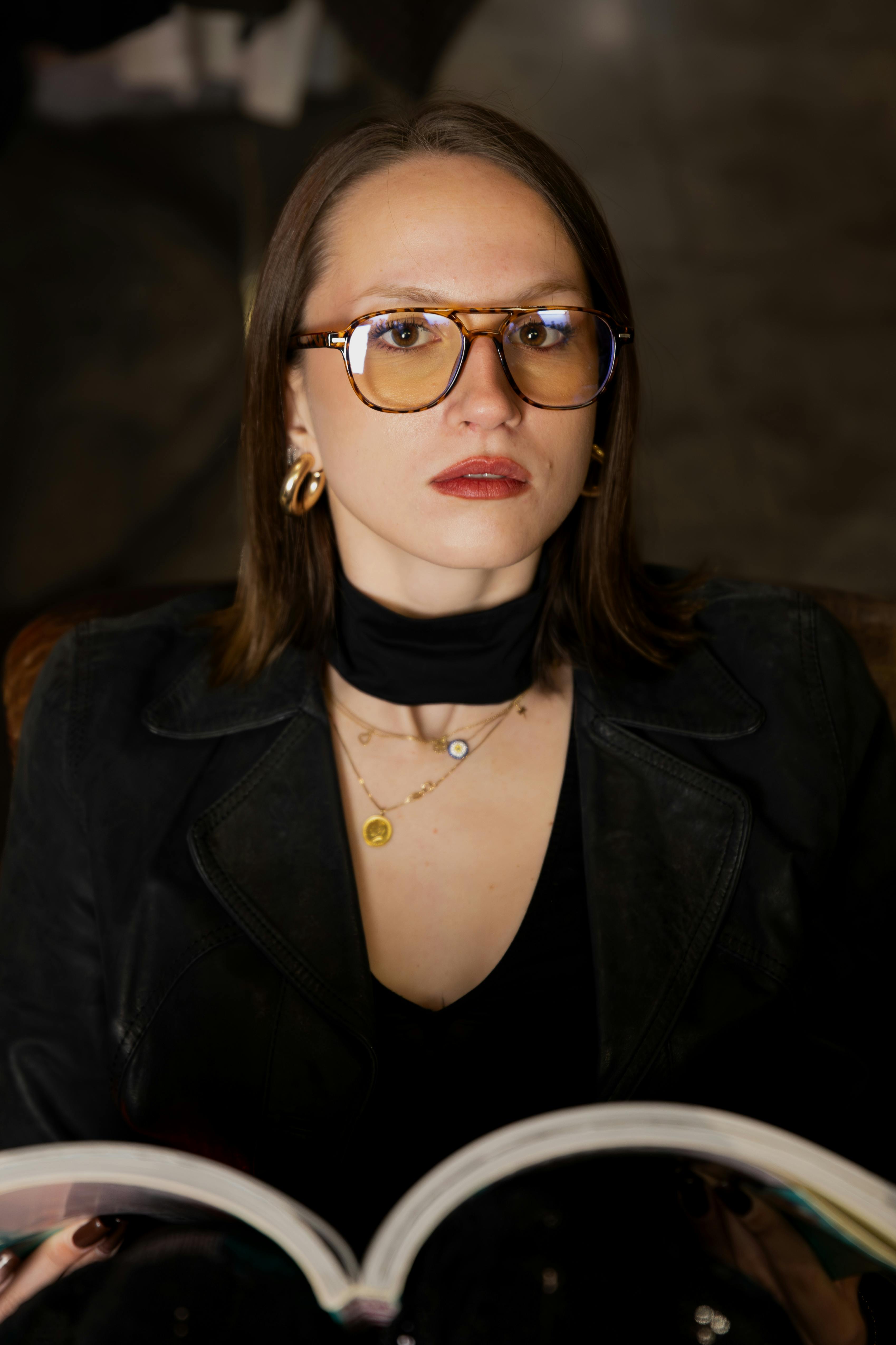 gratis Een geconcentreerde vrouw met bril en trendy kleding is binnenshuis aan het lezen. Stockfoto