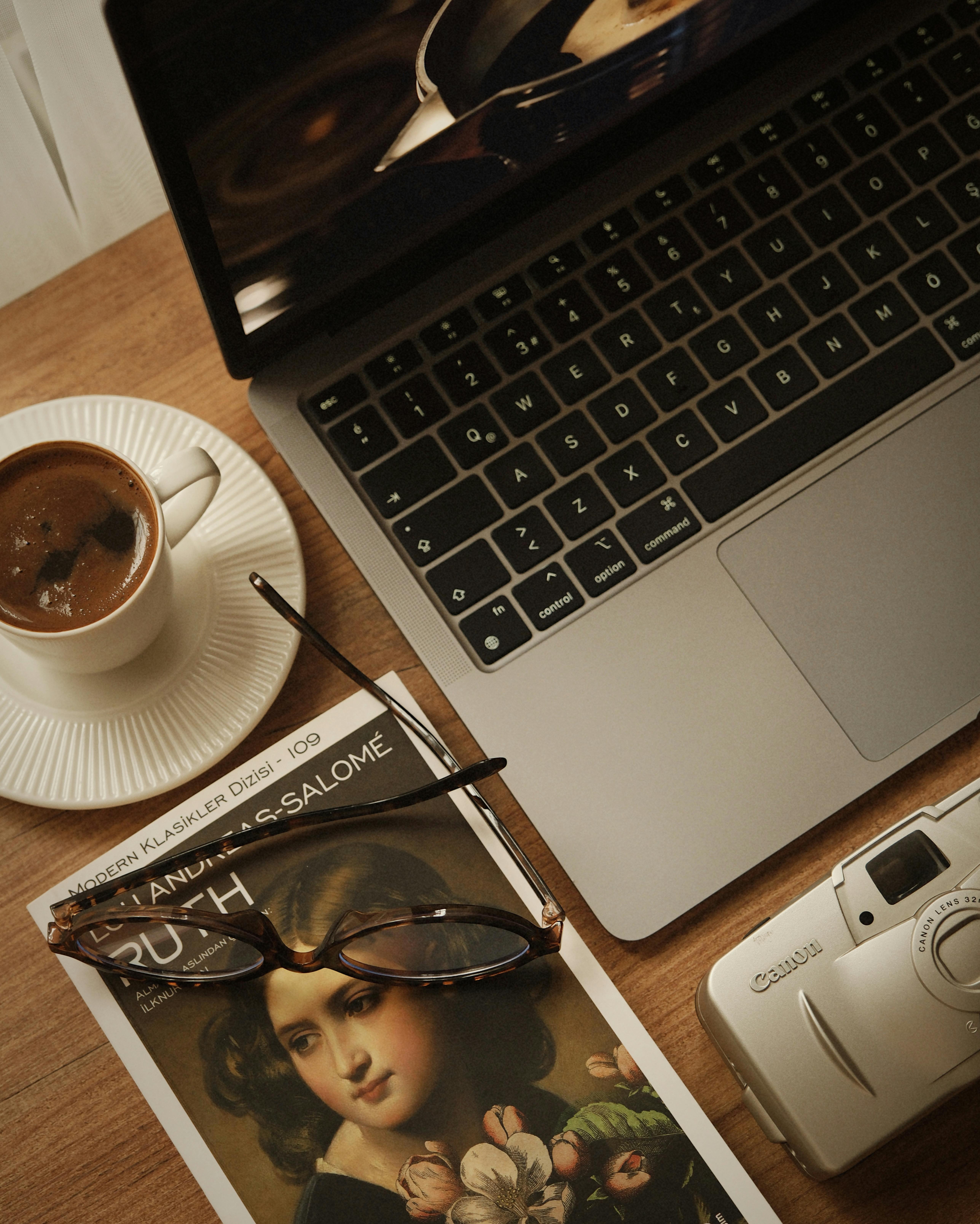 gratis Een ontspannen opstelling met koffie, een boek en een laptop op een houten tafel. Stockfoto