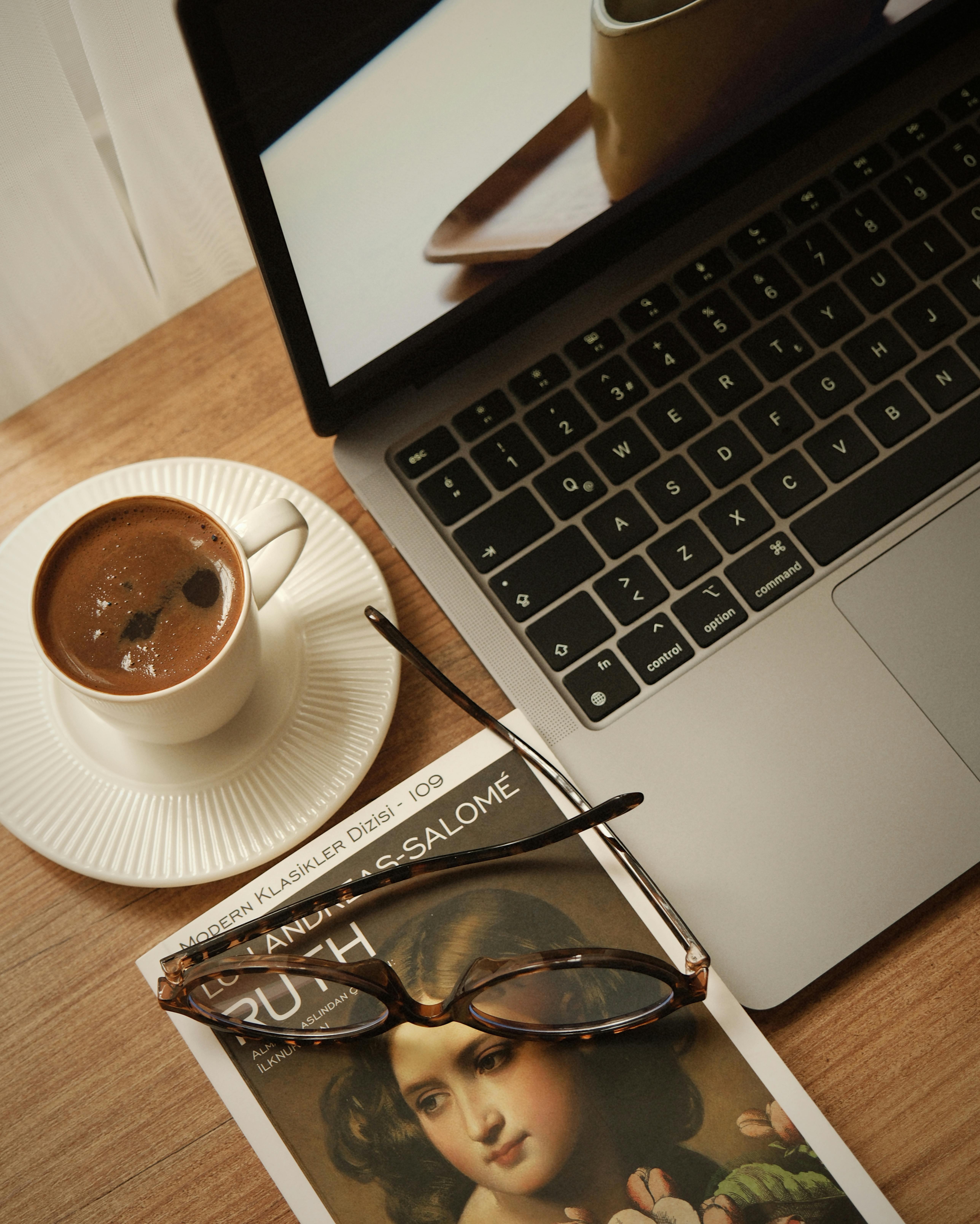 Gratis Uno spazio di lavoro sereno con caffè, un computer portatile e un libro su una scrivania di legno. Foto a disposizione