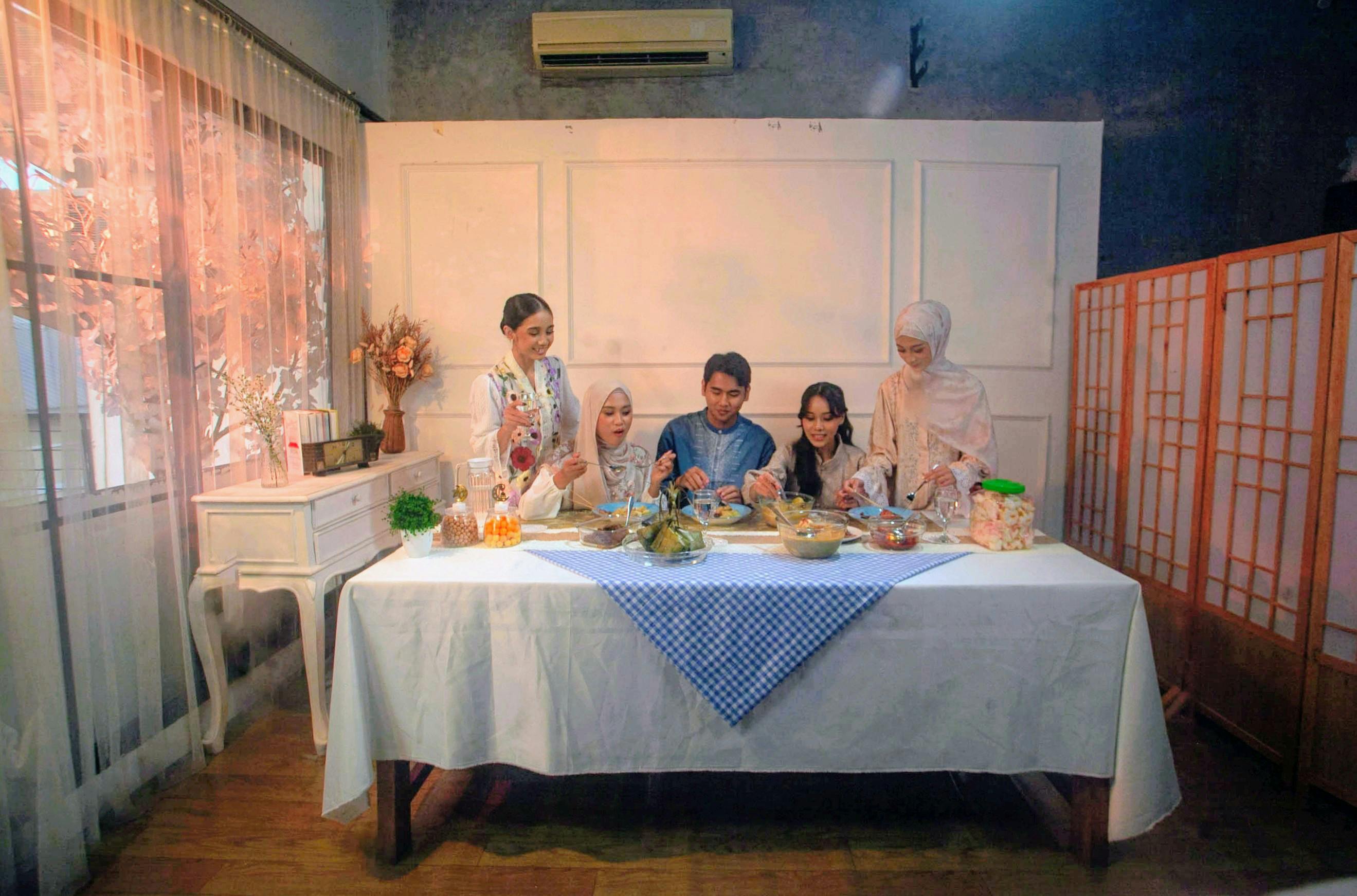 Gratis Sebuah keluarga beranggotakan lima orang menikmati hidangan meriah bersama di dalam rumah, menciptakan suasana hangat dan penuh sukacita. Foto Stok