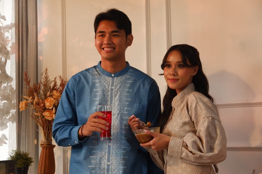 Couple in traditional attire enjoying festive drinks indoors, creating a warm cultural atmosphere.