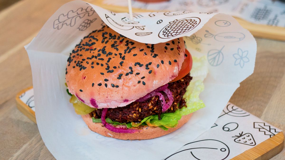 Dark beet quinoa patty with lettuce, tomato and pickled onion in a pink sesame bun