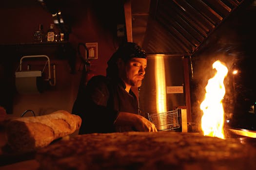 Portrait of a chef cooking in a warm, dimly lit kitchen, with a dramatic open flame.