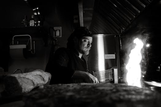 A chef skillfully prepares food over an open flame in a commercial kitchen, black and white.